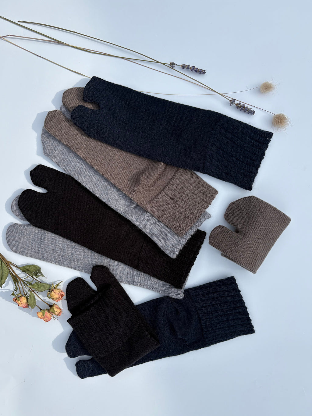 Flat lay of ankle length tabi split-toe socks in black, dark navy, brown, taupe, and grey — warm knit Japanese tabi socks styled with dried lavender and roses wool blend