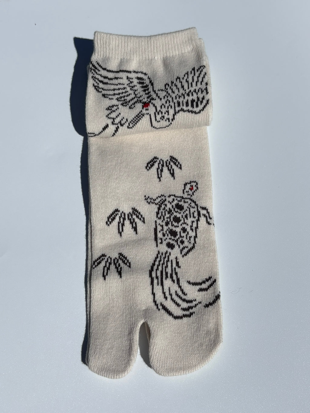 Tabi sock with crane, turtle and leaf design on a light gray background
