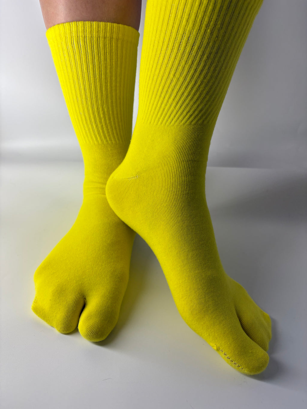 yellow tabi split toe socks with ribbed cuff crew length worn on white background