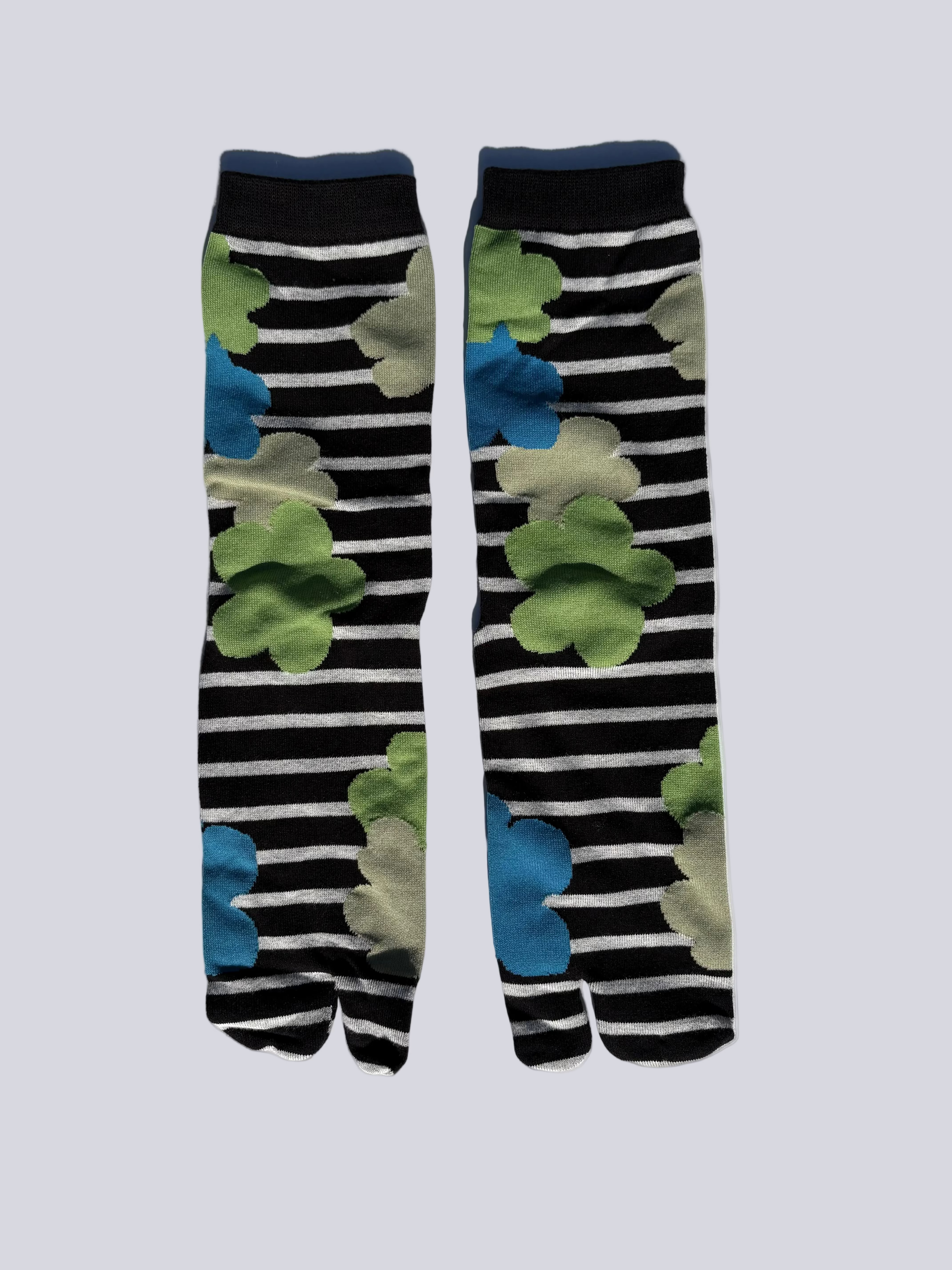 Pair of tabi japanese split toe socks with black and white stripes and green and blue abstract patterns on a light gray background