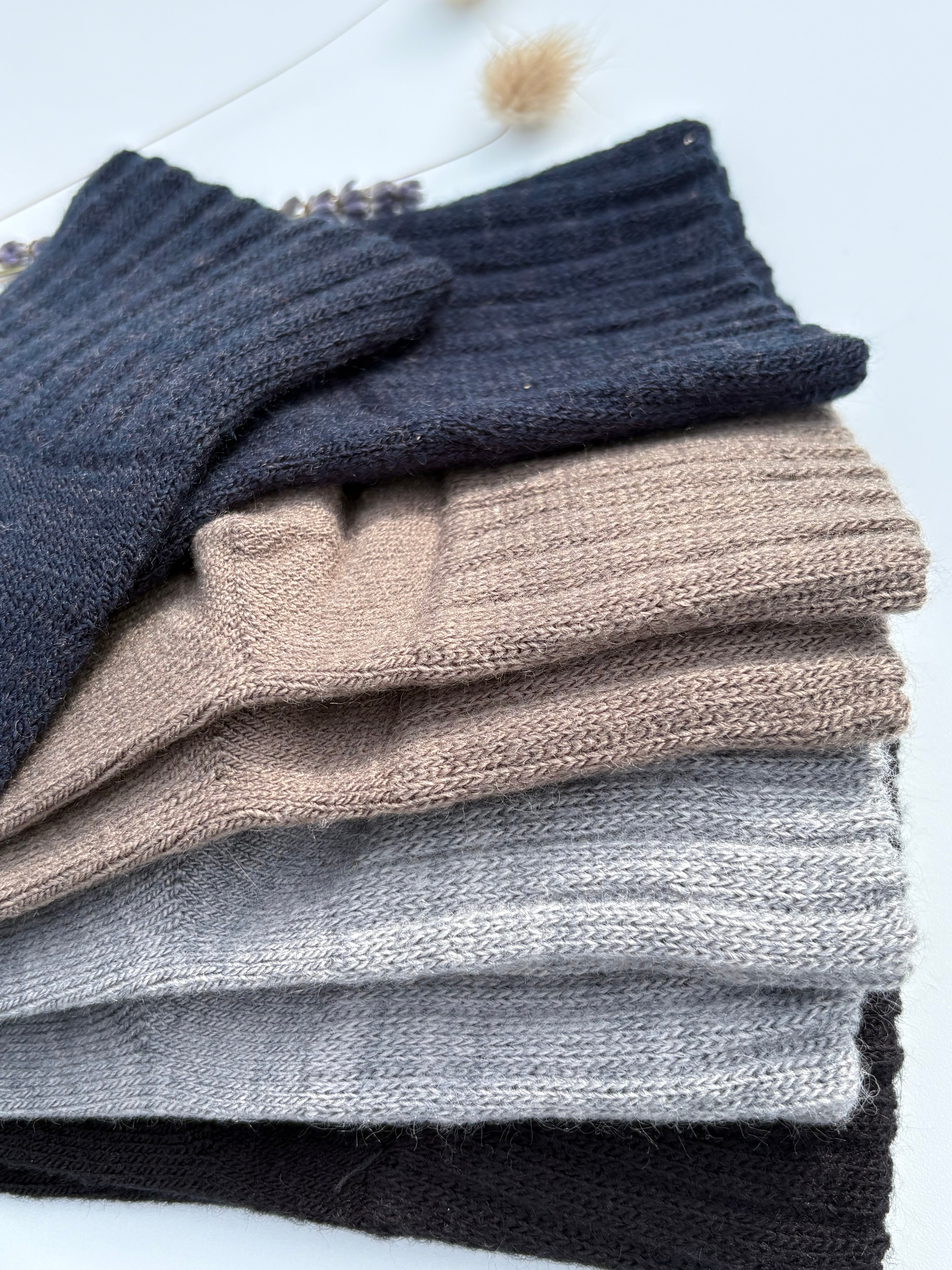 Close-up of stacked tabi split-toe sock legs showing soft fuzzy knit texture in charcoal, light grey, taupe, and navy — warm winter tabi socks with brushed wool-like finish