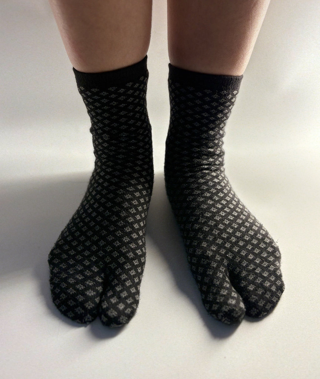 Black tabi split-toe socks with grey diamond (hishi) pattern worn on feet — Japanese hishi pattern tabi socks styled on bare legs