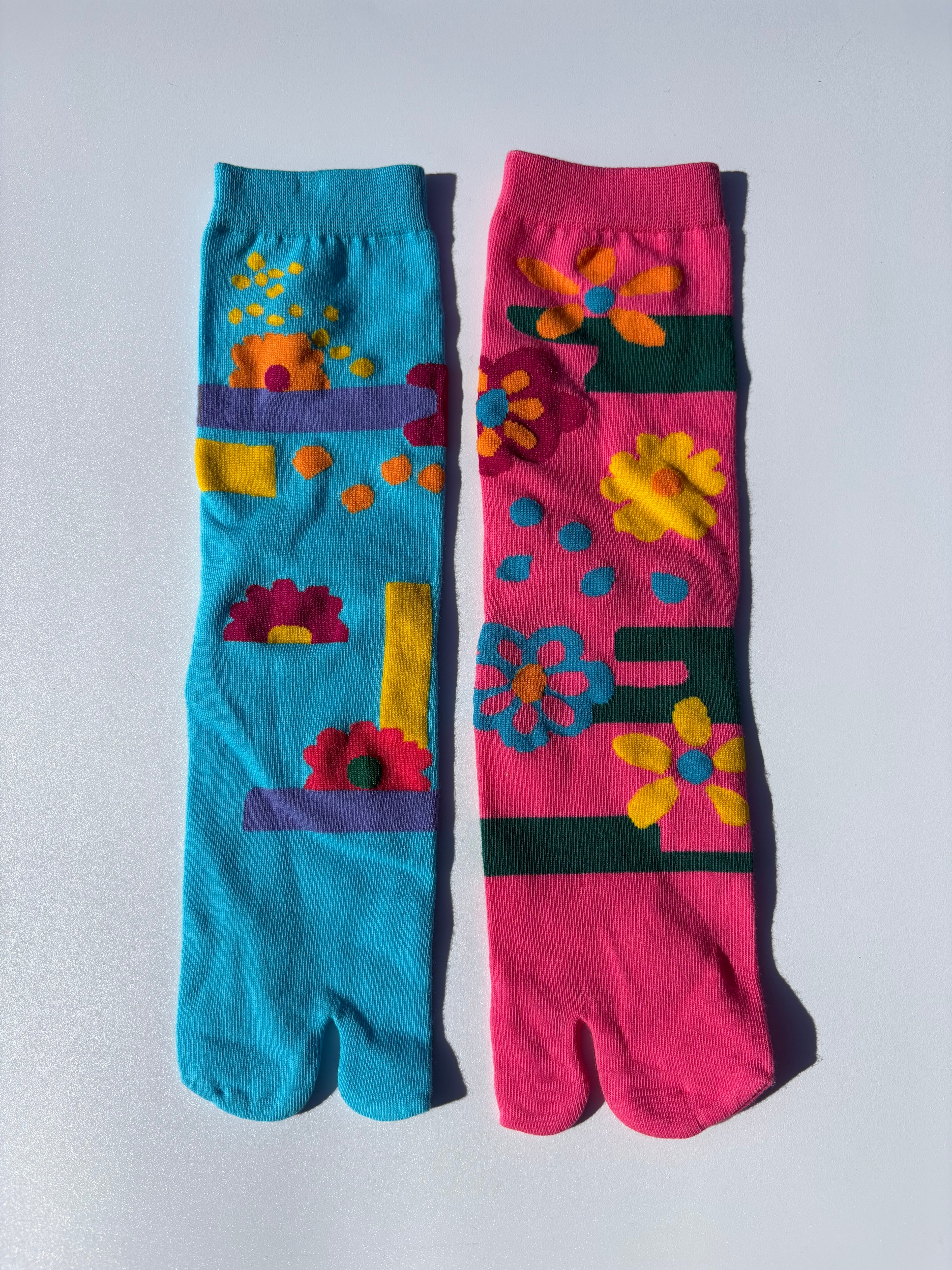 Colorful tabi socks with floral bold pop art neon pink and blue floral patterns on a light gray background