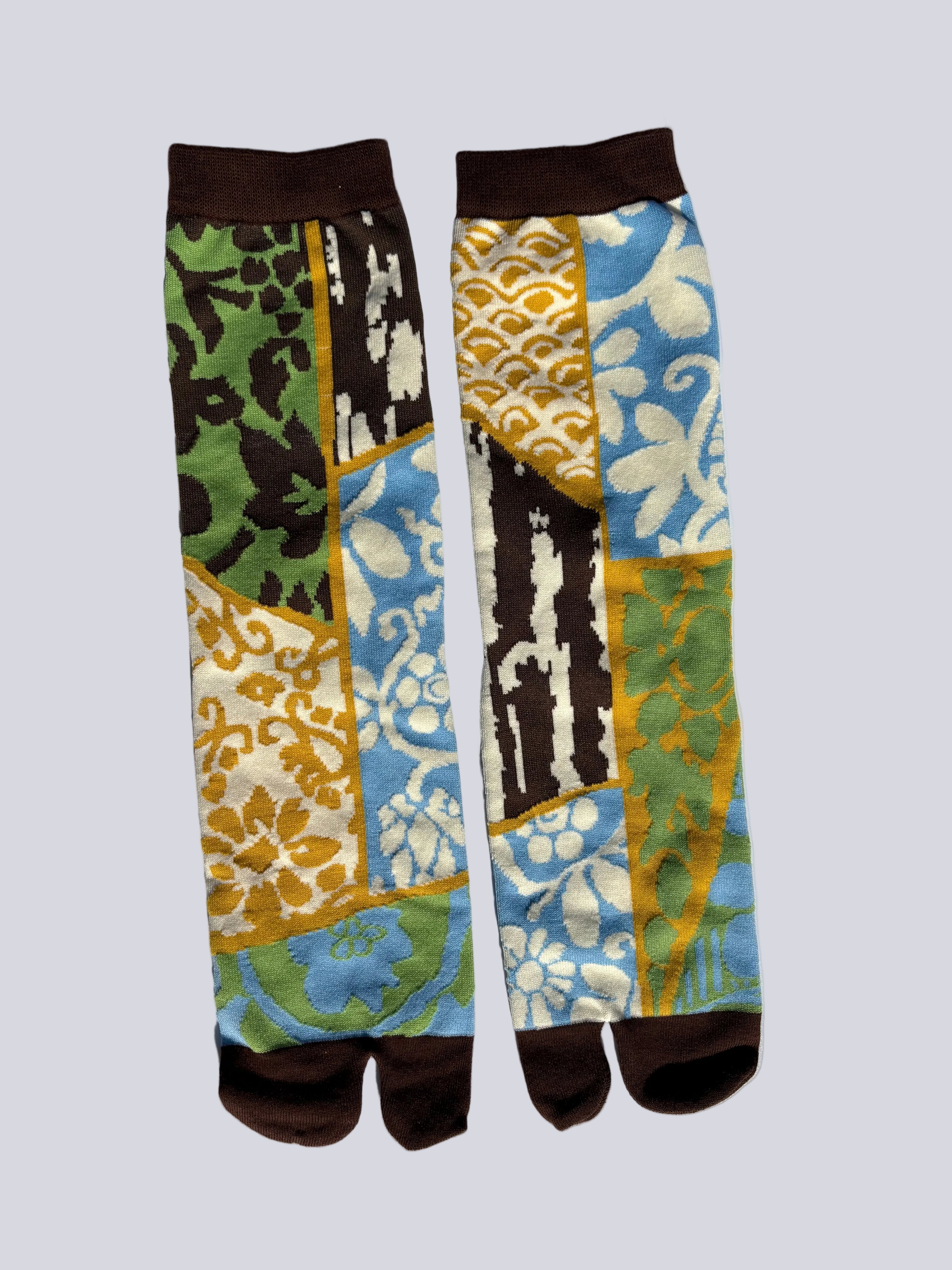 Tabi split-toe socks with Japanese kimono-inspired patchwork print featuring karakusa, seigaiha, ikat, and floral motifs in blue, green, and gold — brown cuff