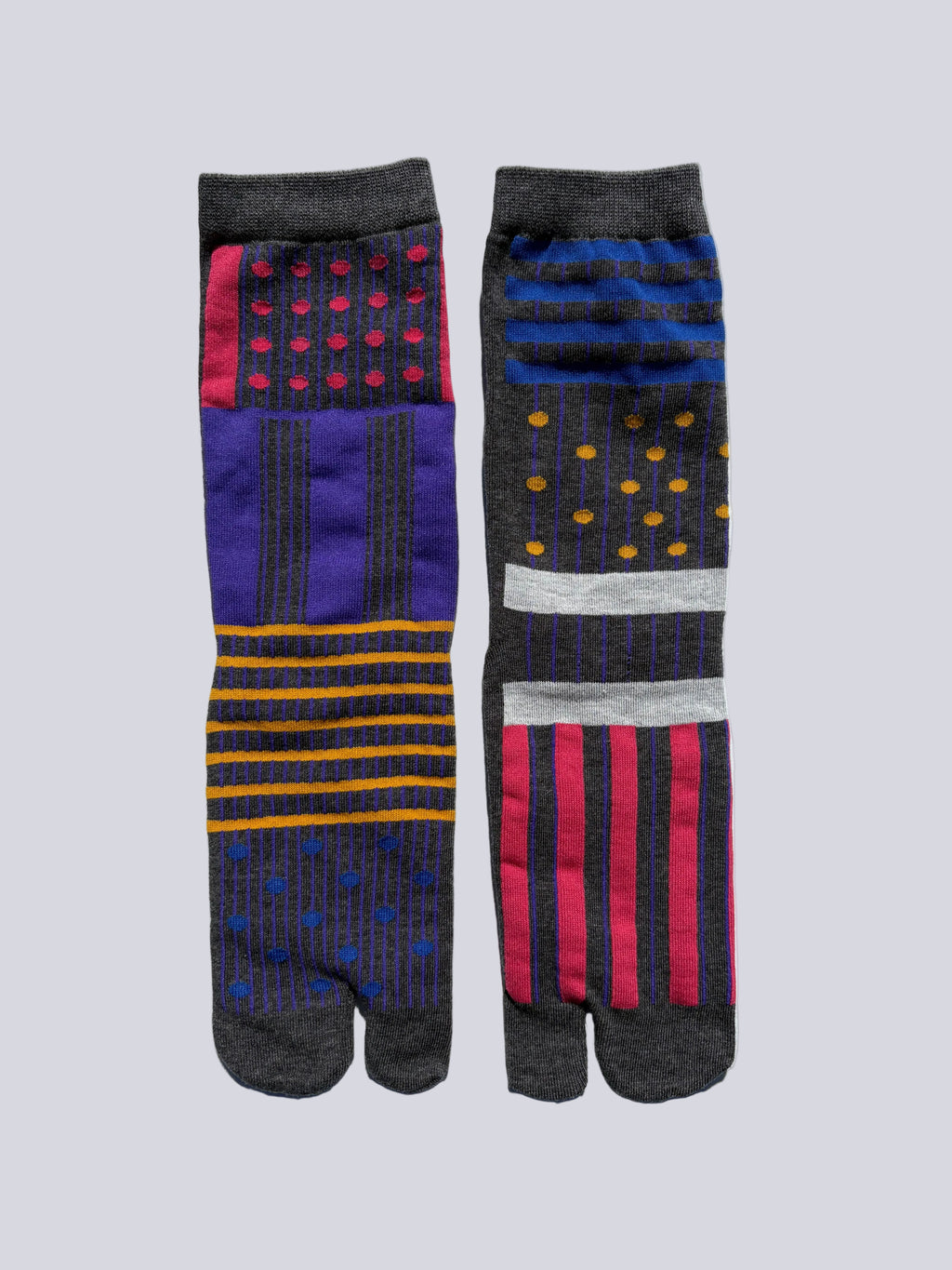 Two pairs of patterned tabi socks with playful mix of colour block panels, polka dots, and bold stripes on a light gray background