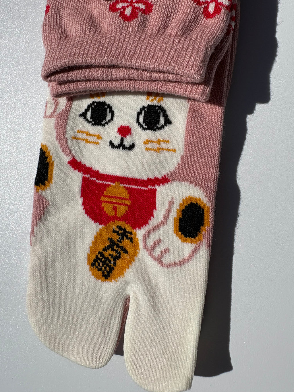 close up of Pink tabi split-toe socks with maneki-neko lucky cat print and red floral pattern — Japanese-made novelty lucky cat tabi socks (足袋)