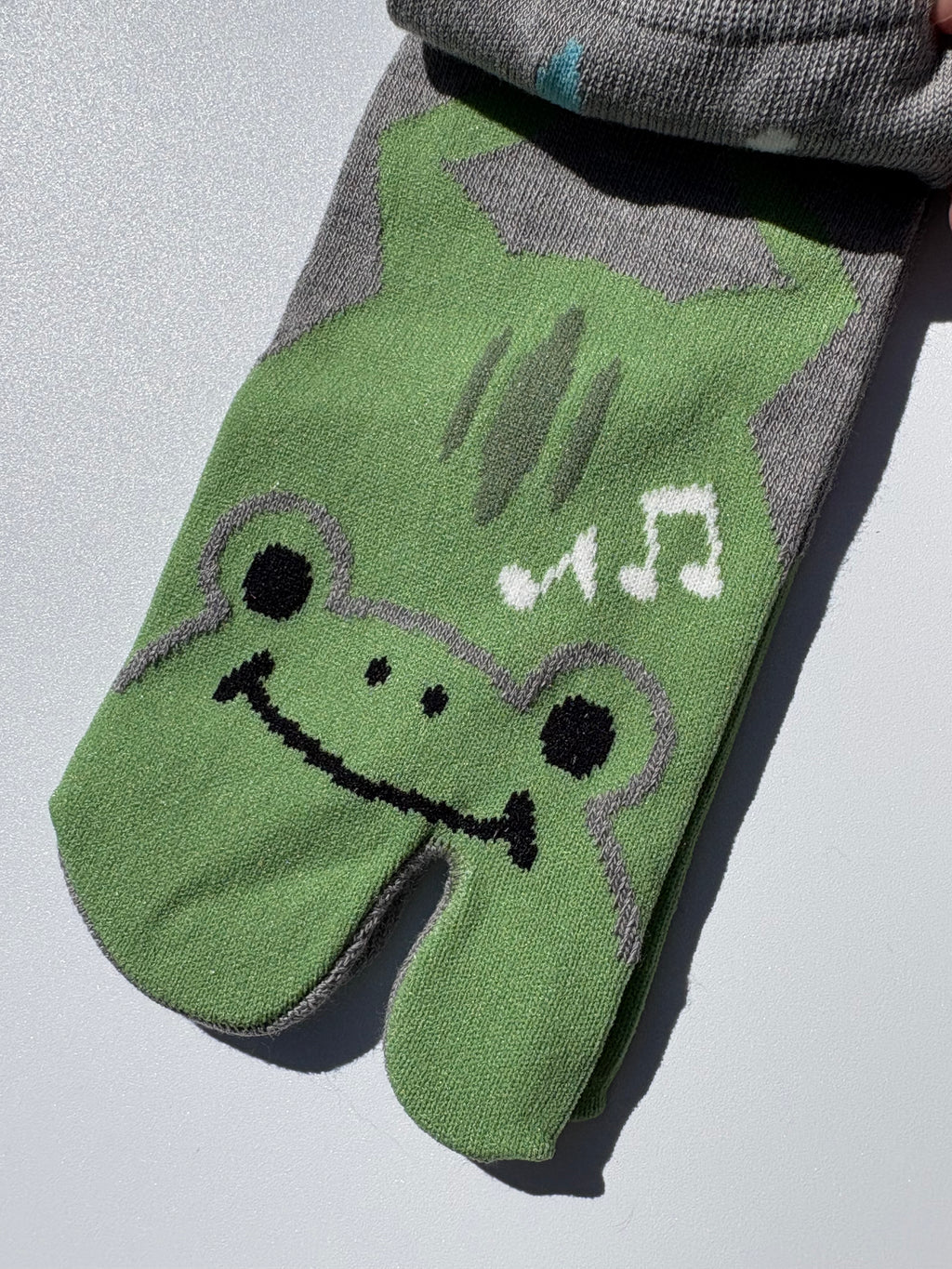 close-up of green tabi split-toe sock toe showing kawaii frog face wearing headphones with music notes — Japanese novelty animal tabi socks