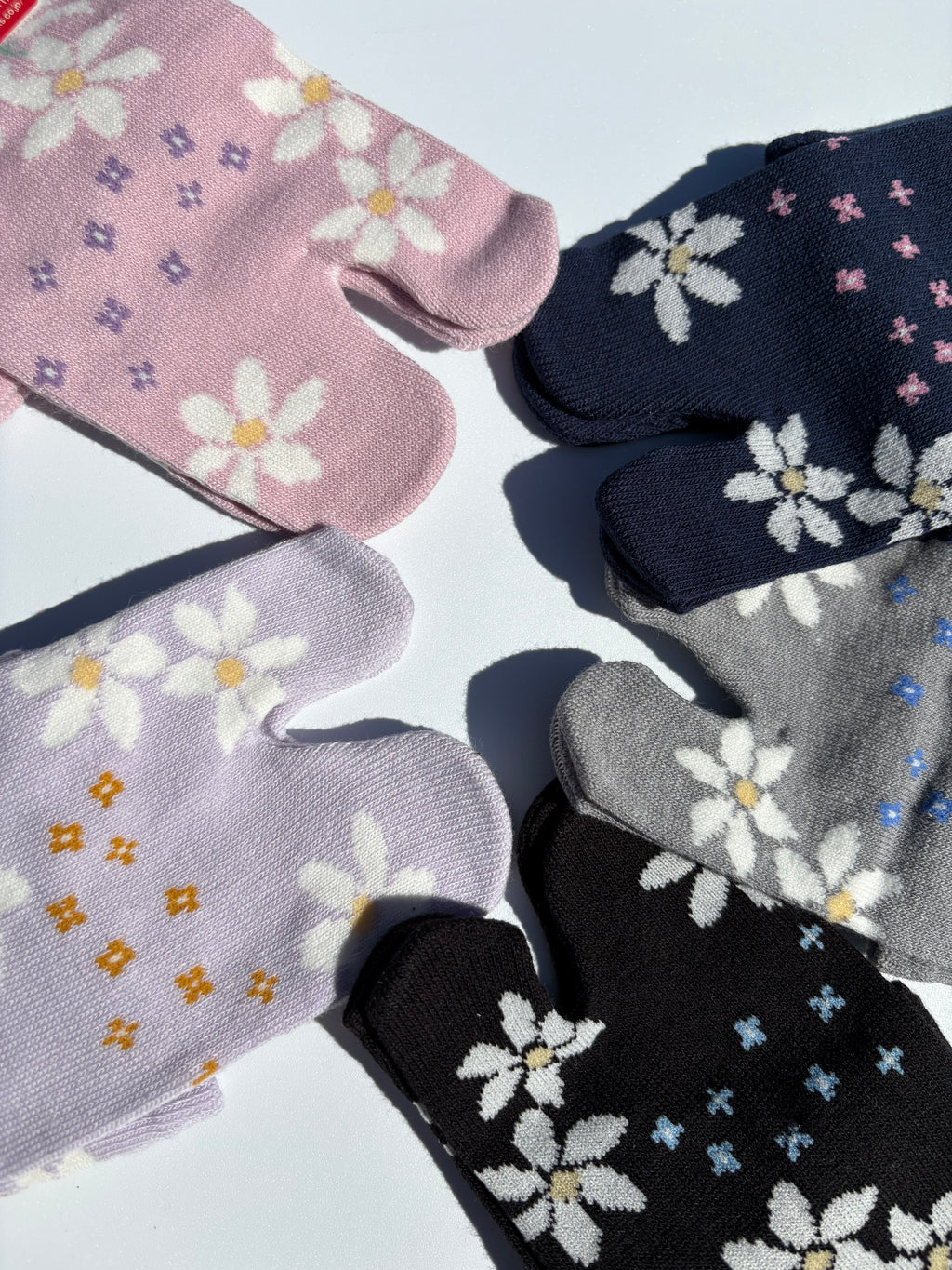 close up of sakura print tabi socks in cotton blend on a white surface - various colours showing of pink navy charcoal grey black and lilac