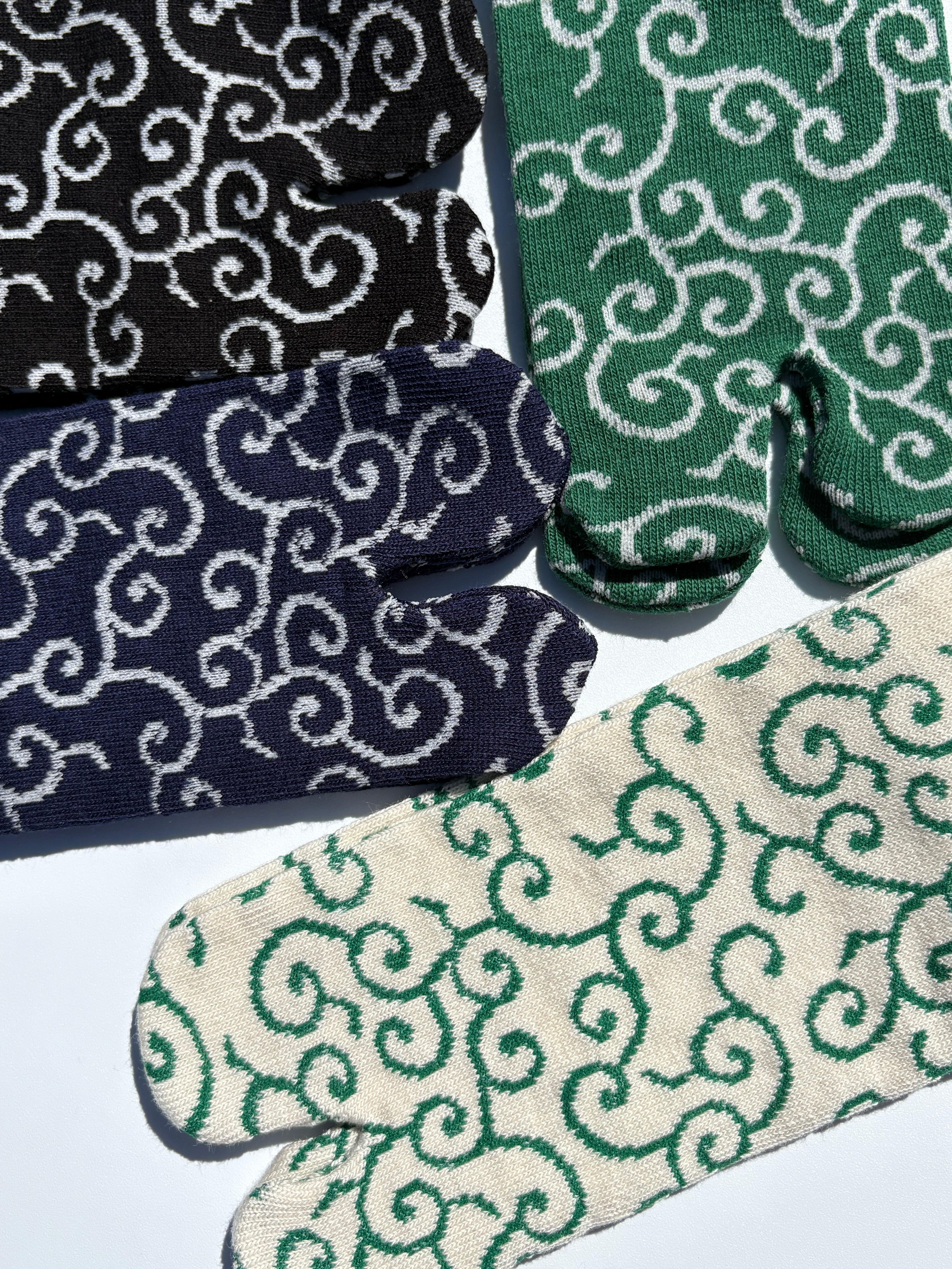 Close-up of tabi split-toe sock toes showing traditional Japanese karakusa arabesque scroll pattern in black, navy, forest green, and cream colourways
