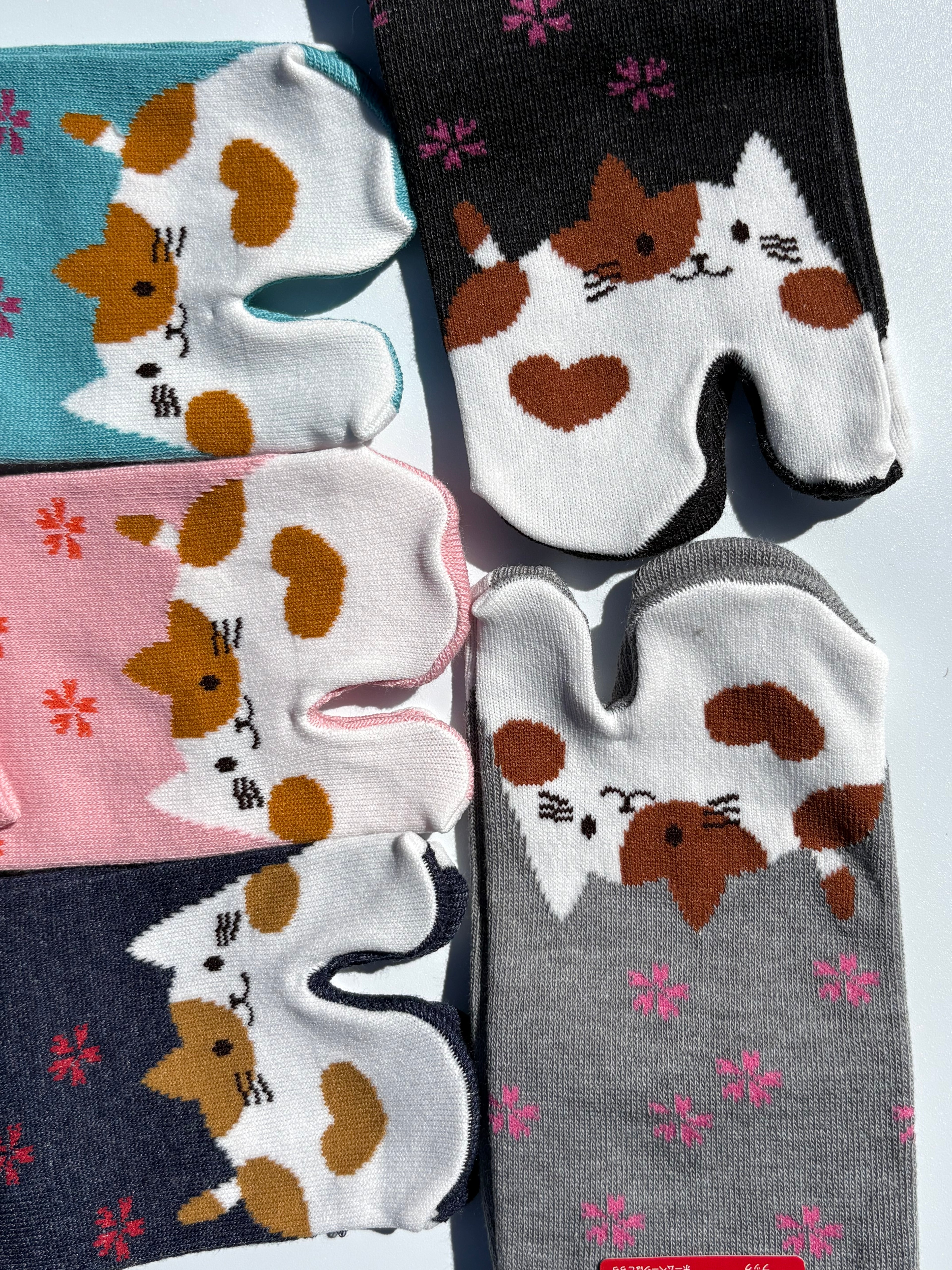 Close-up of tabi split-toe sock toes showing calico cat face design in teal, pink, navy, and grey with pink snowflake print — Japanese novelty cat tabi socks