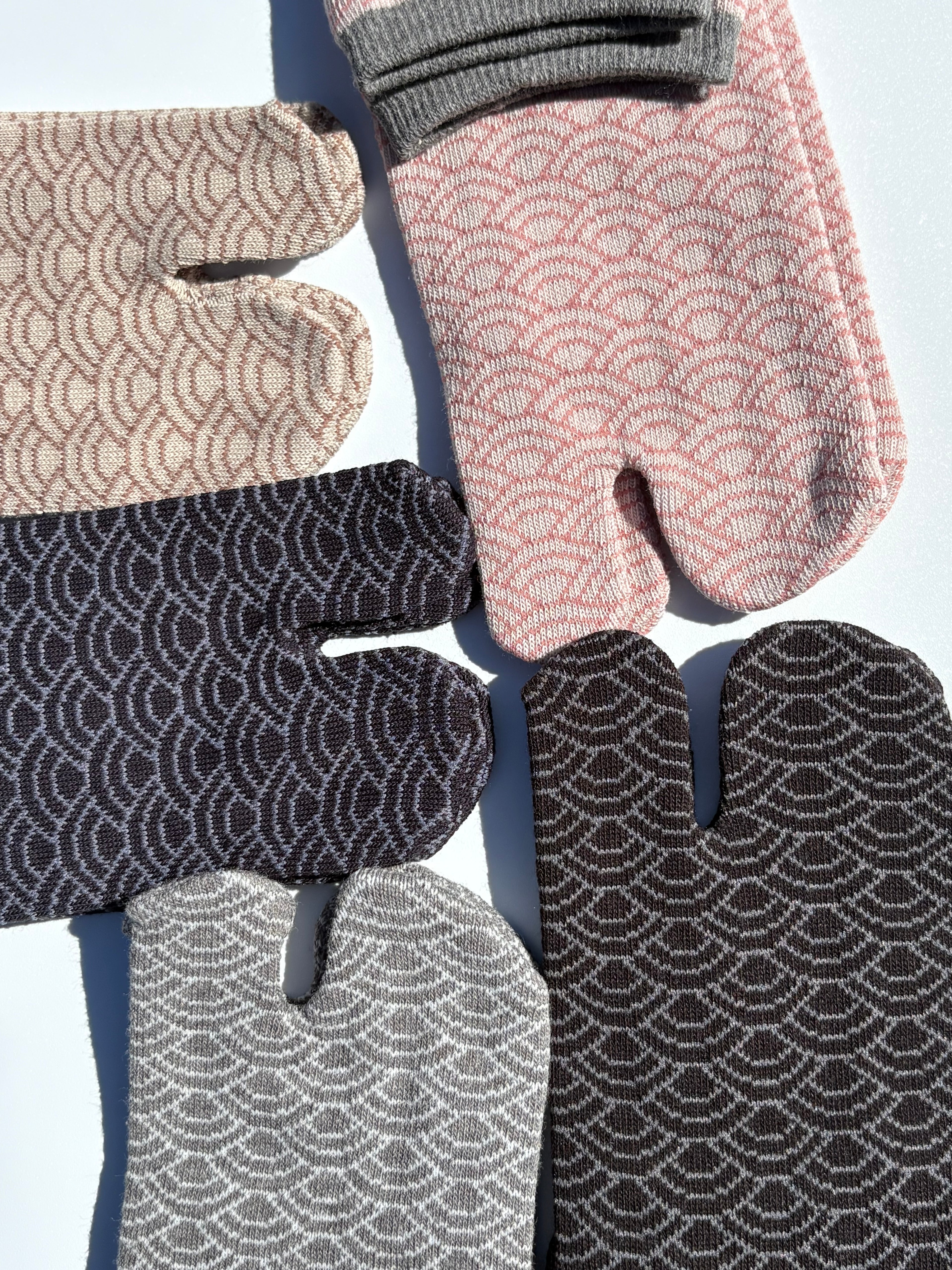 close up of five pairs of tabi split-toe socks in traditional Japanese seigaiha wave pattern — black with rust, black with grey, taupe, pink and grey with red cuff — Omotenashi Selection Gold Award made in Japan