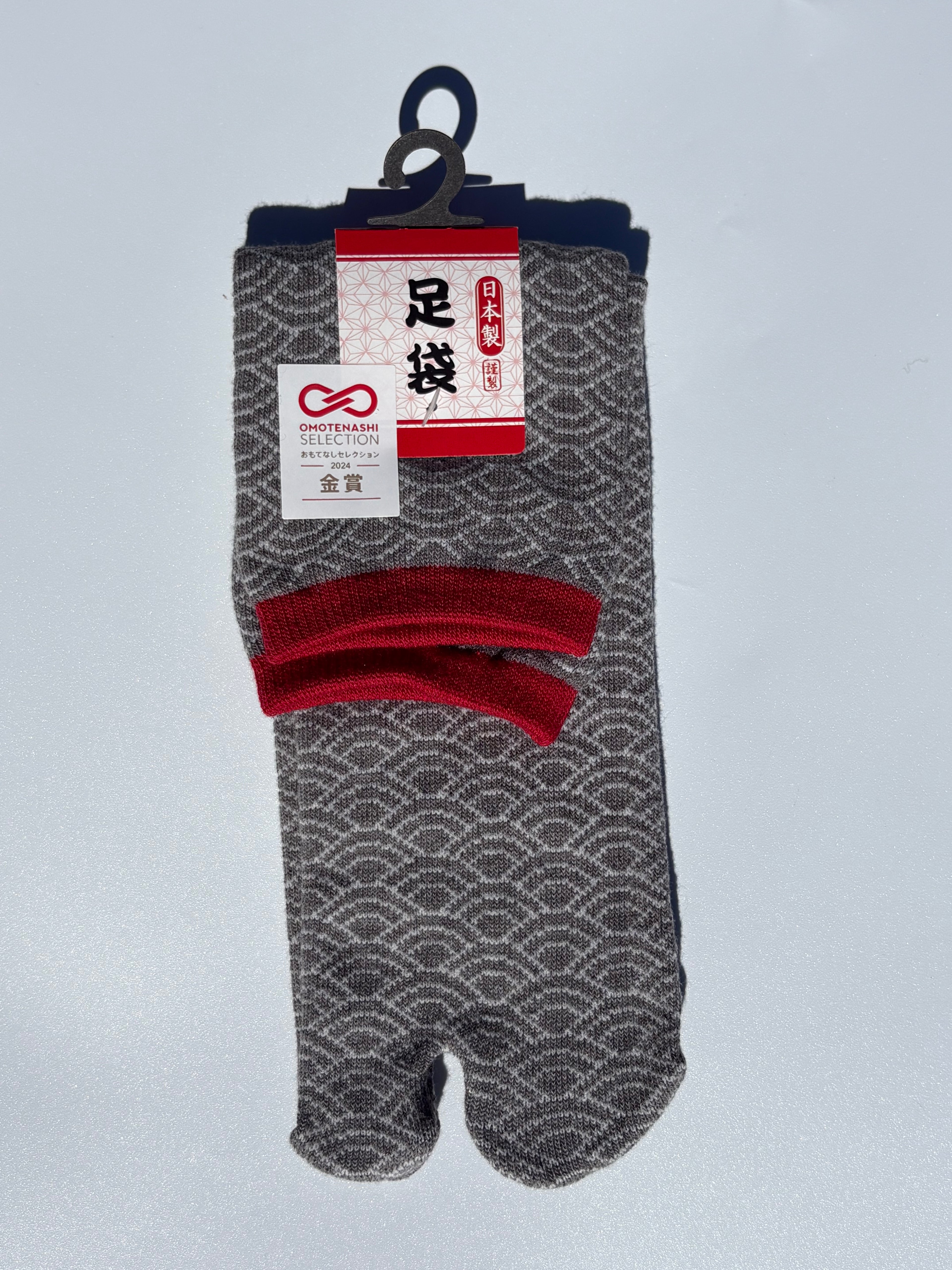 Pair of grey seigeiha print tabi socks in red accents with a pattern on a light gray background