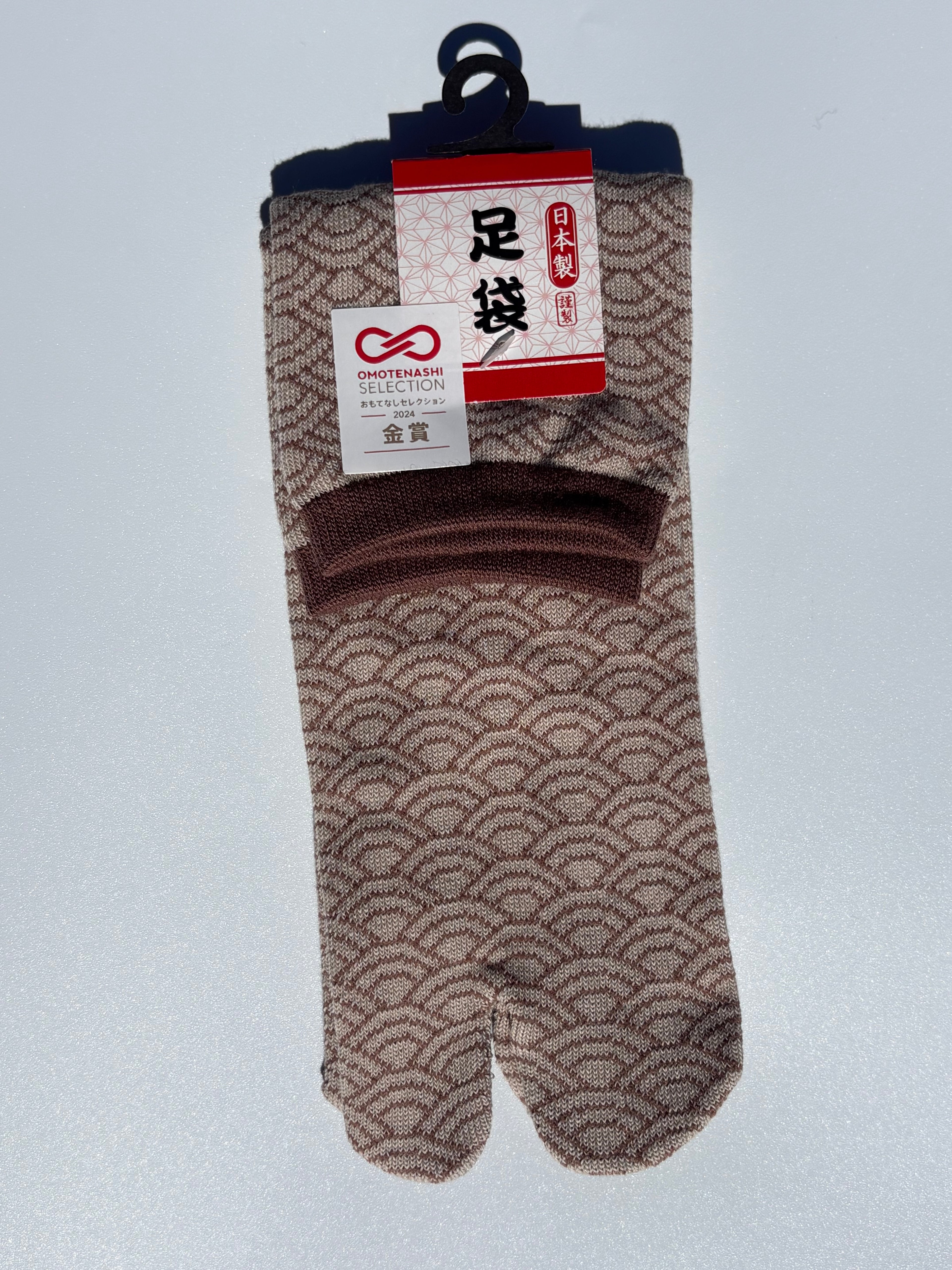 Pair of beige seigeiha print tabi socks in dark brown accents with a pattern on a light gray background
