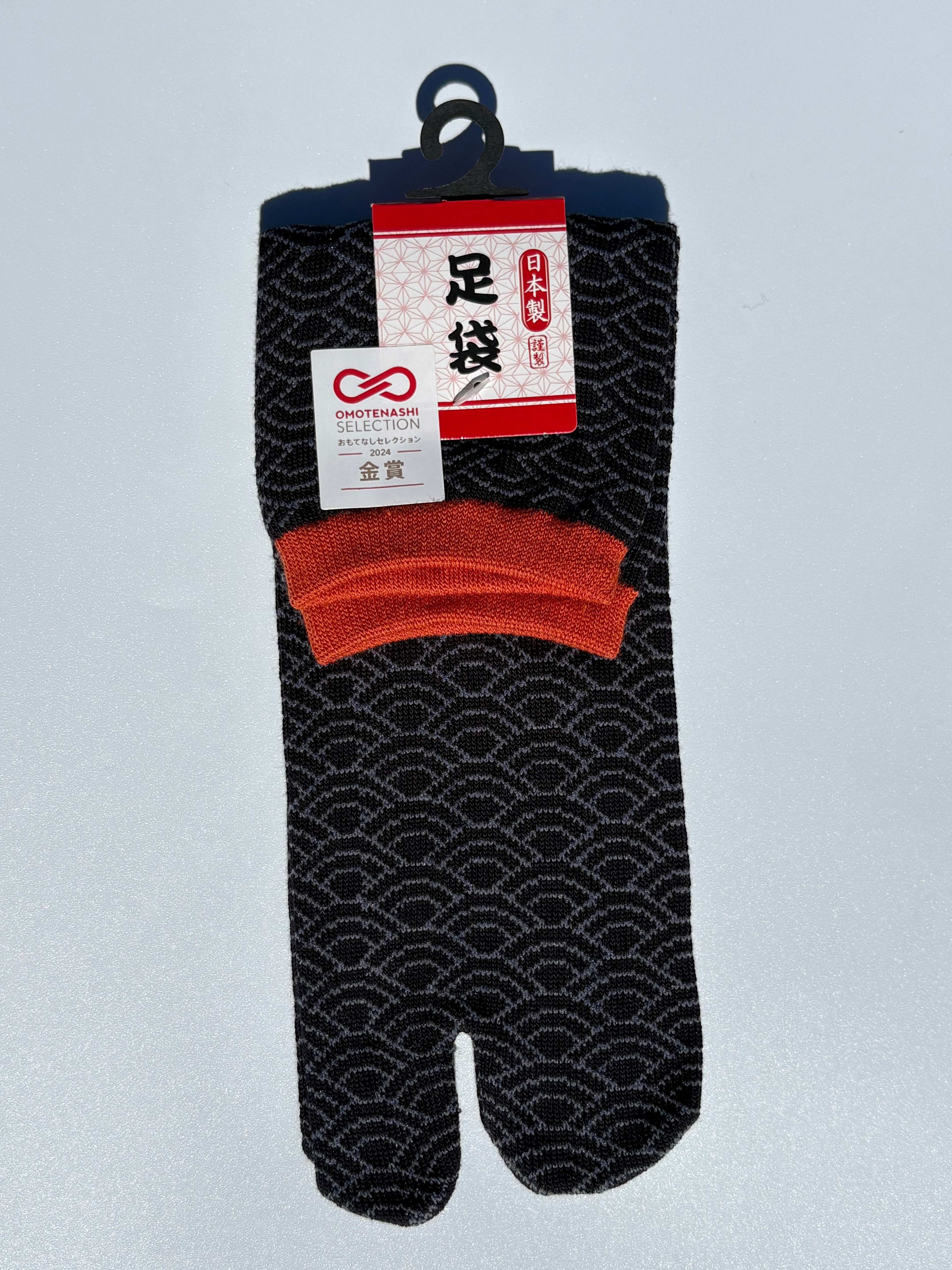 Pair of seigeiha print tabi socks in black white orange accents with a pattern on a light gray background