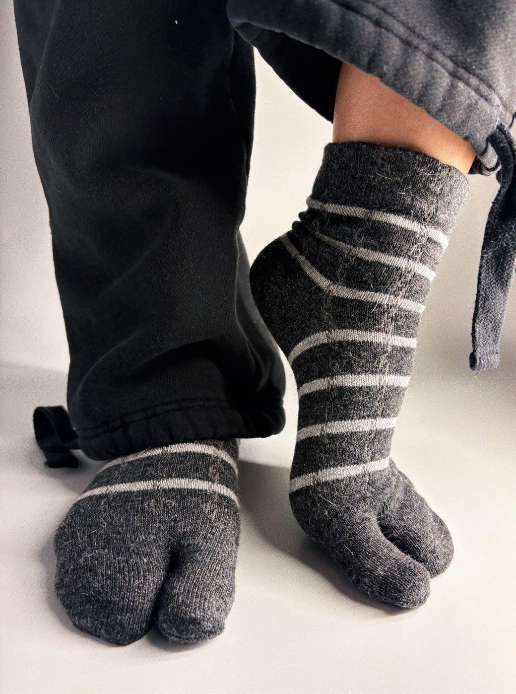 Charcoal grey striped tabi split-toe socks worn on feet with black jogger pants — slouchy knit Japanese tabi socks styled with wide-leg trousers
