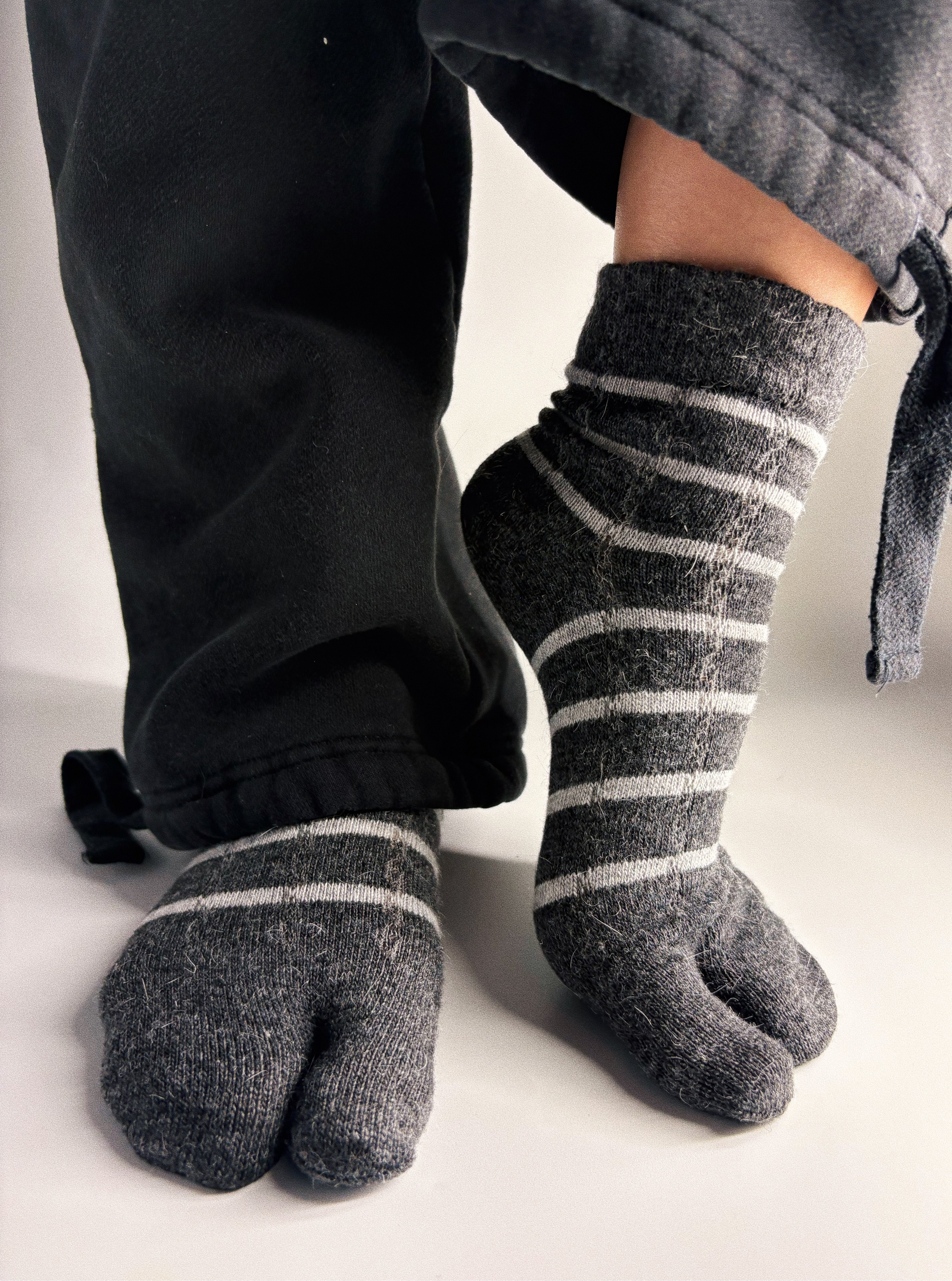 Charcoal grey striped tabi split-toe socks worn on feet with black jogger pants — slouchy knit Japanese tabi socks styled with wide-leg trousers