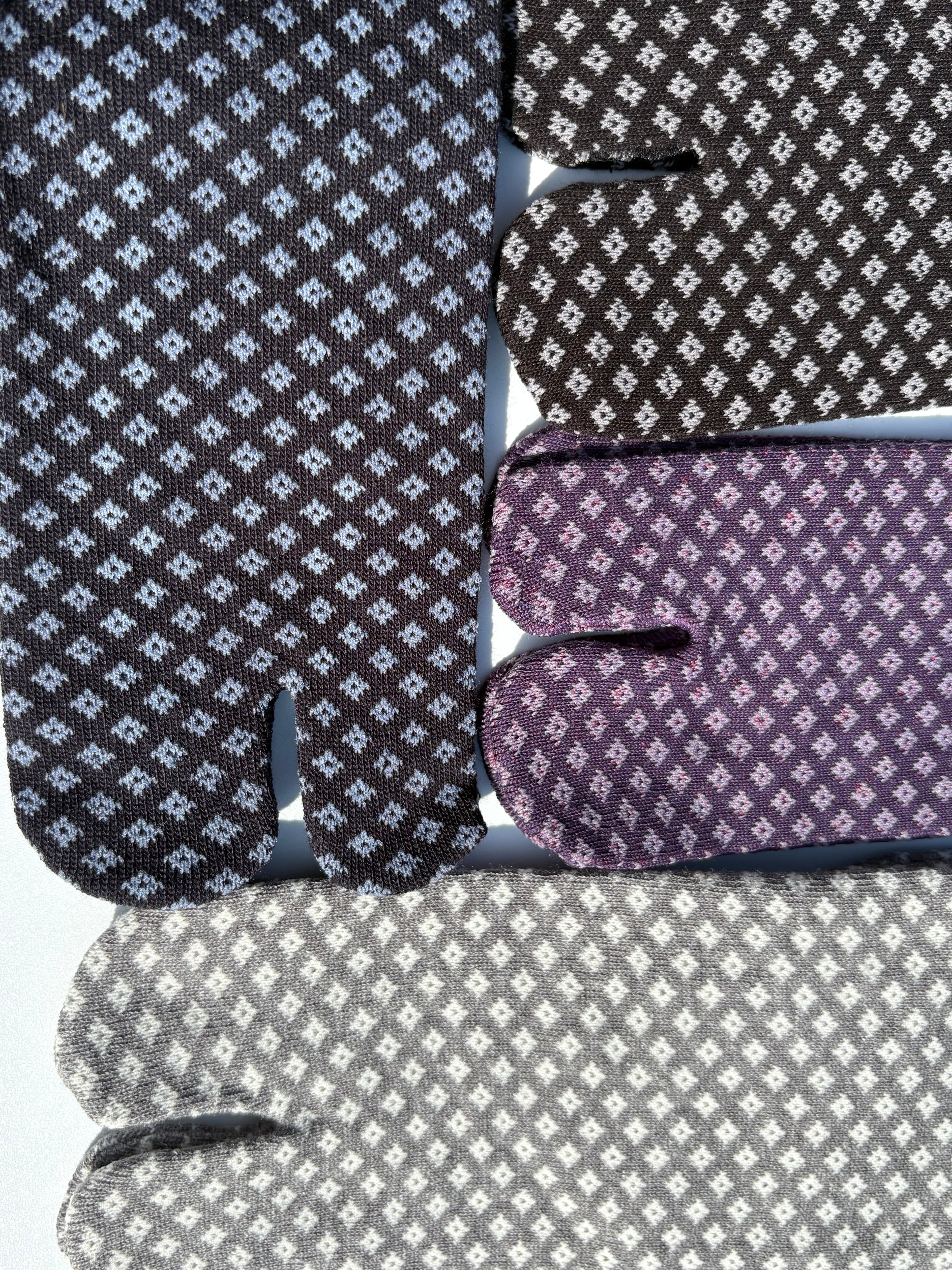 Close-up of tabi split-toe sock toes showing traditional Japanese diamond (hishi) pattern in dark grey, purple, and light grey colourways