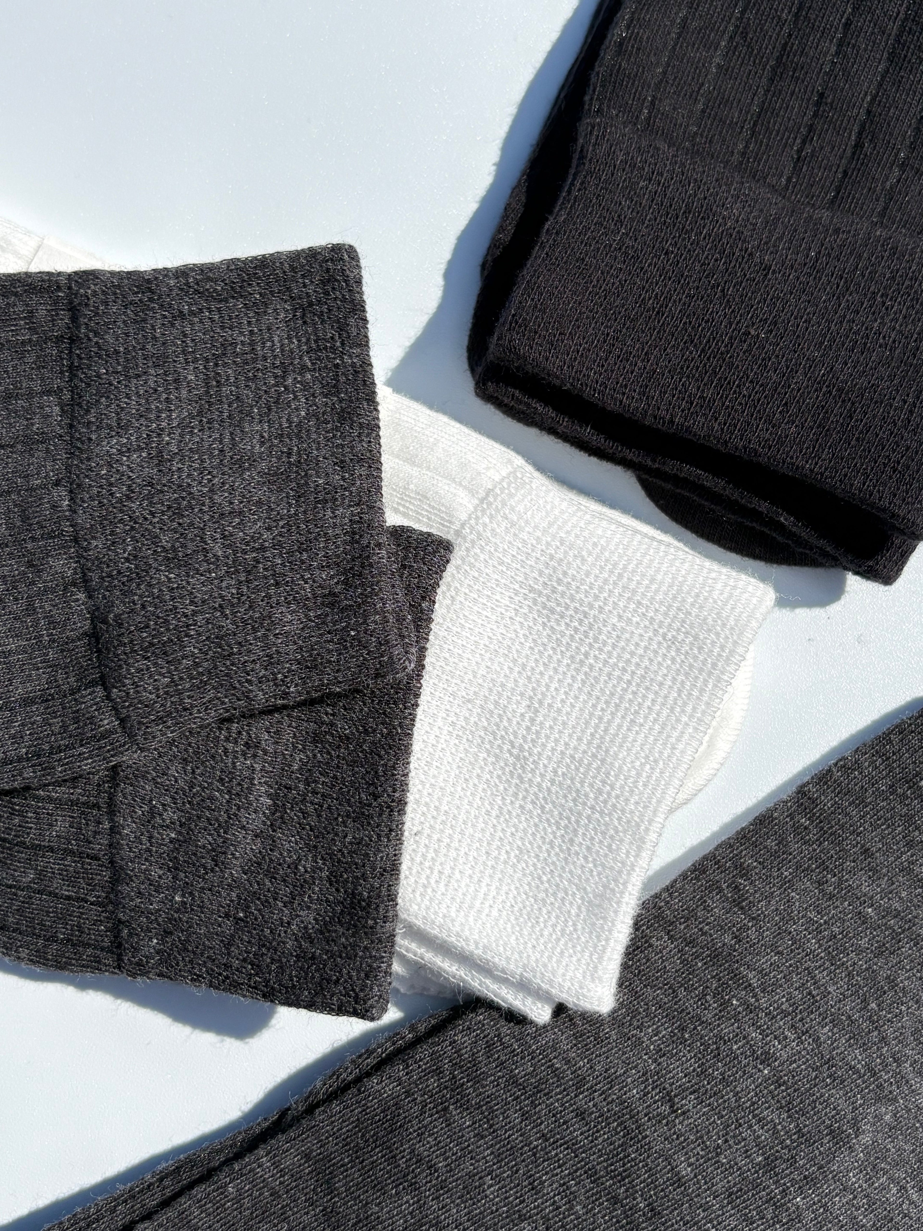 Close-up flat lay of ribbed tabi split-toe socks in charcoal grey, white waffle-knit, and black — Japanese tabi sock texture detail