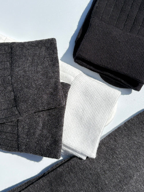 Close-up flat lay of ribbed tabi split-toe socks in charcoal grey, white waffle-knit, and black — Japanese tabi sock texture detail