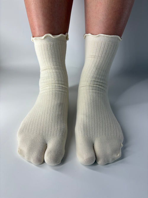 Cream ribbed socks with lightly lettuce edged cuff worn on feet against a neutral background