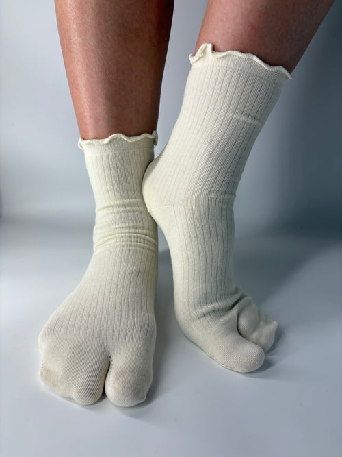 Cream ribbed socks with lightly lettuce edged cuff worn on feet against a neutral background