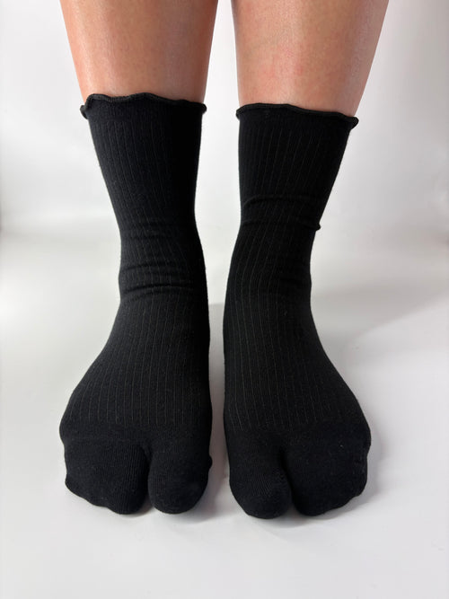 Black ribbed socks with lightly lettuce edged cuff worn on feet against a white background