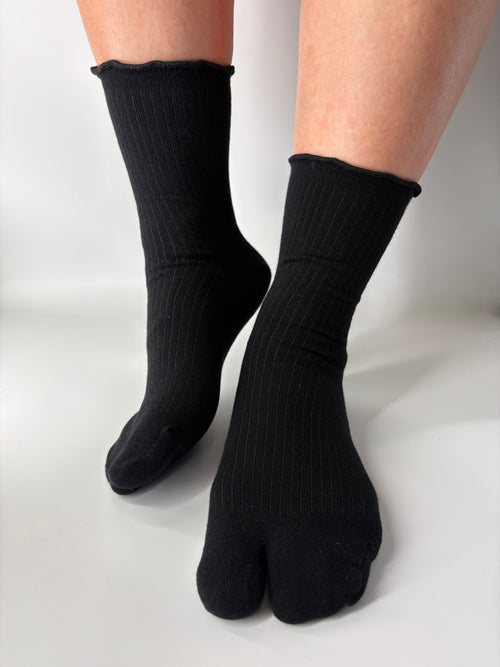 Black ribbed socks with lightly lettuce edged cuff worn on feet against a white background
