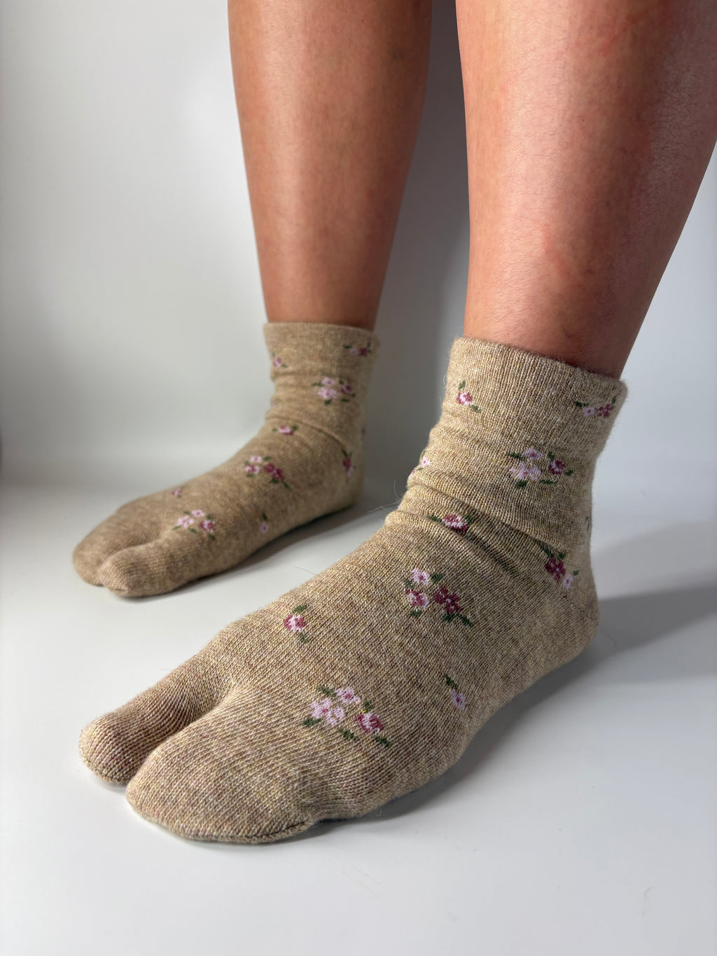 Beige split toe tabi socks with floral patterns worn by a person on a white background