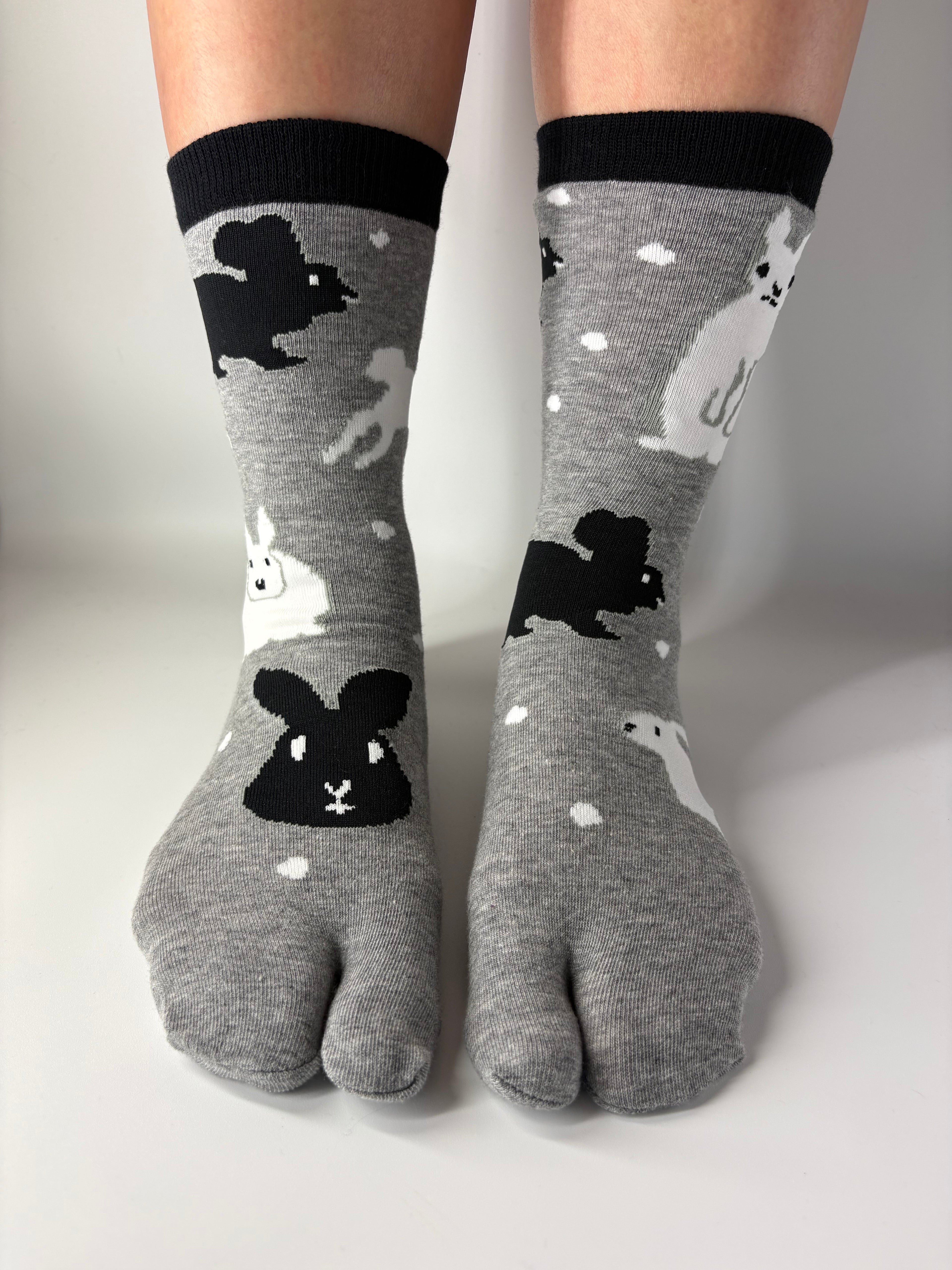 Grey crew socks with a black and white bunny rabbit print pattern, worn on a person's feet against a plain white background.