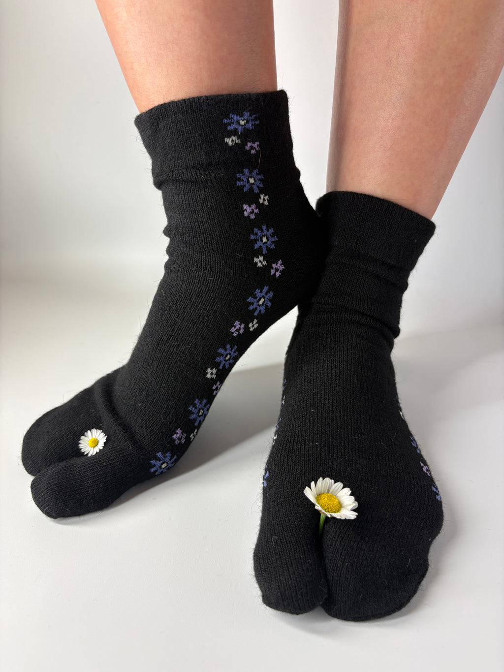 A pair of black tabi socks with small daisy and blue flower patterns, shown on feet against a plain white background.