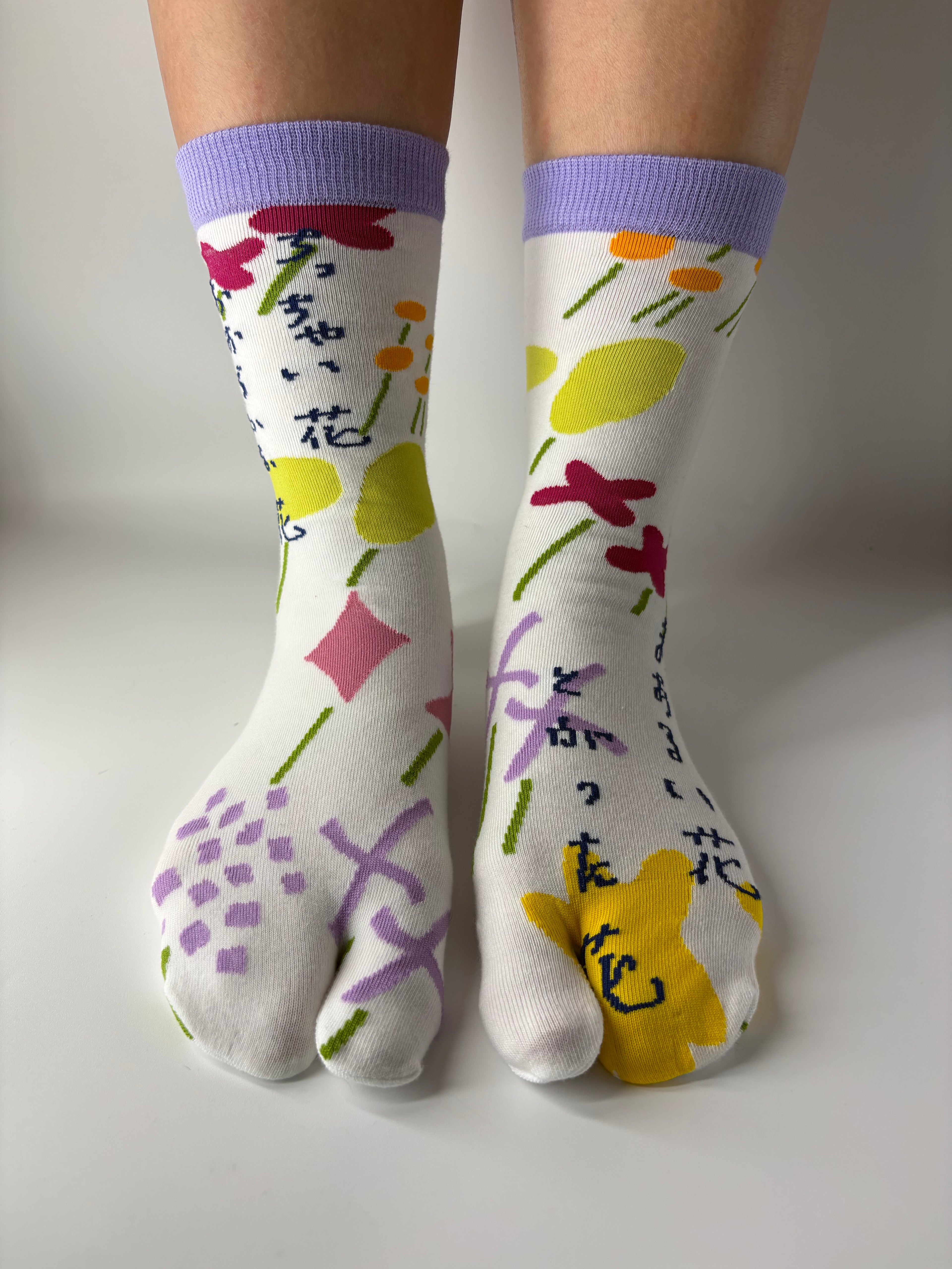 View of fun multi coloured abstract graphic print on white base socks , standing on a white floor with a split toe japanese sock design. Sock is made of cotton natural fibres
