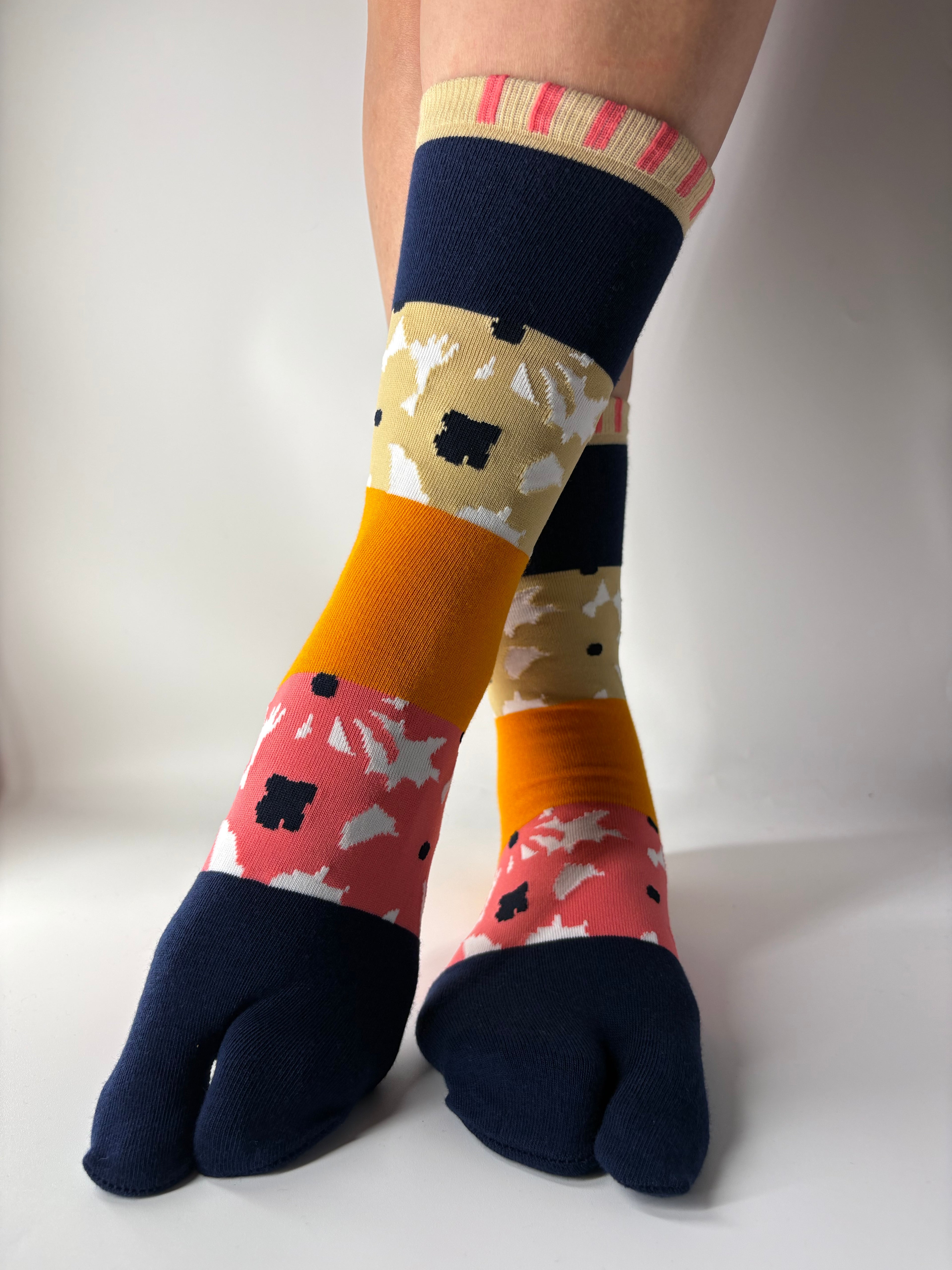 Tabi Co. patchwork tabi socks in navy, mustard, pink and khaki floral pattern, worn on legs against white background