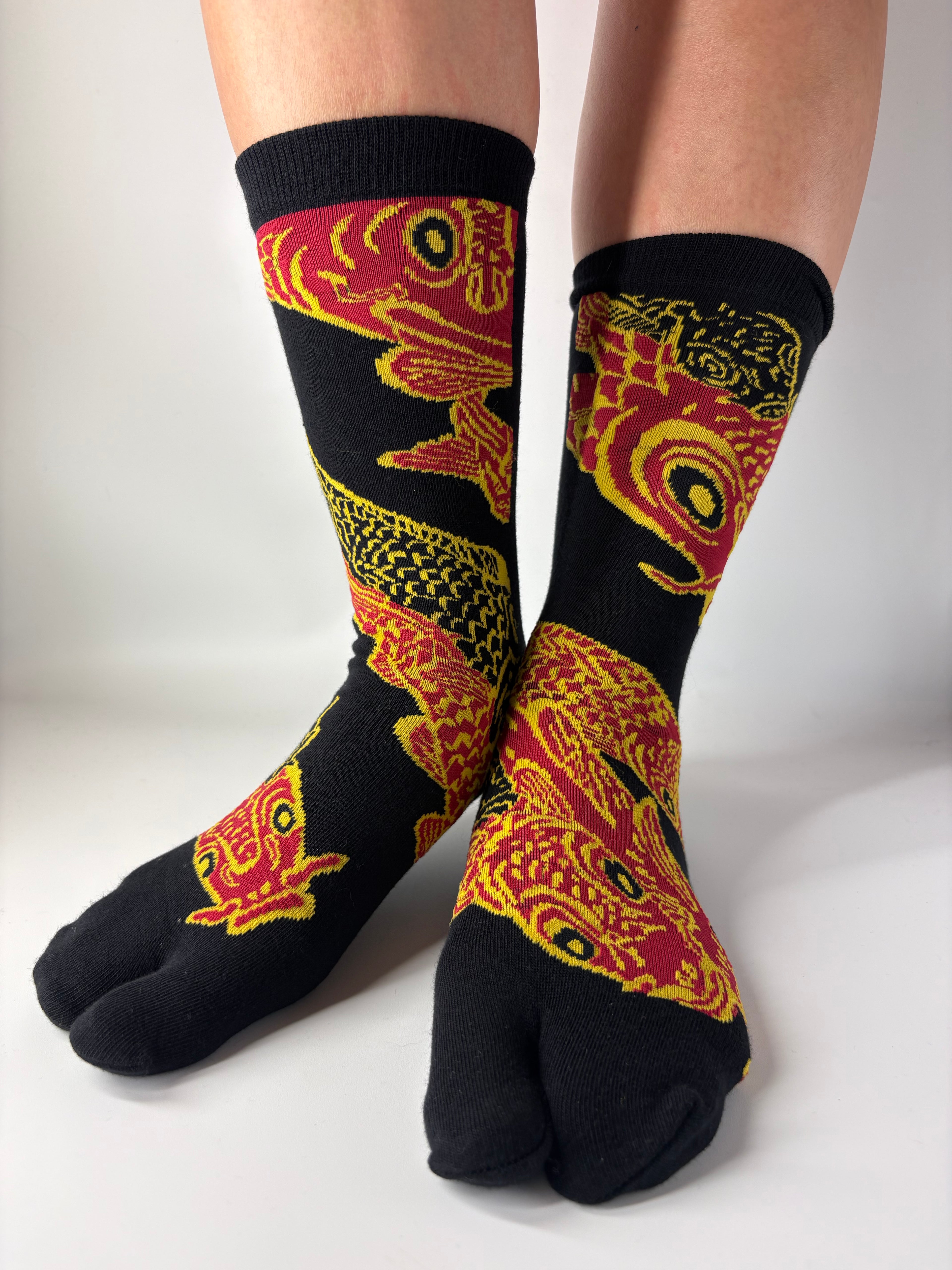 Black socks with red and yellow fish pattern worn by a person on a white background