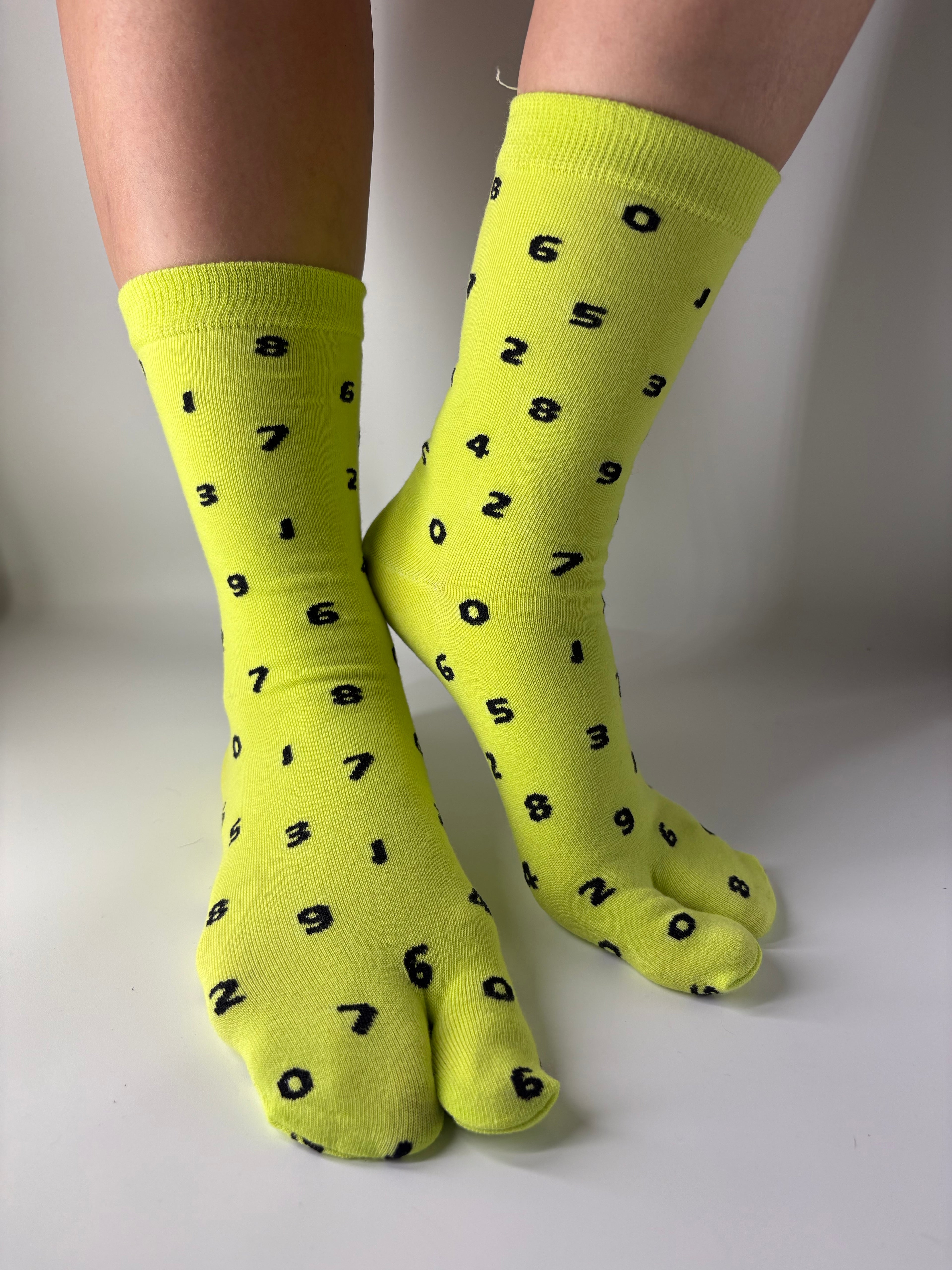 Tabi Co. neon yellow split toe cotton socks with a scattered black number print, worn on feet