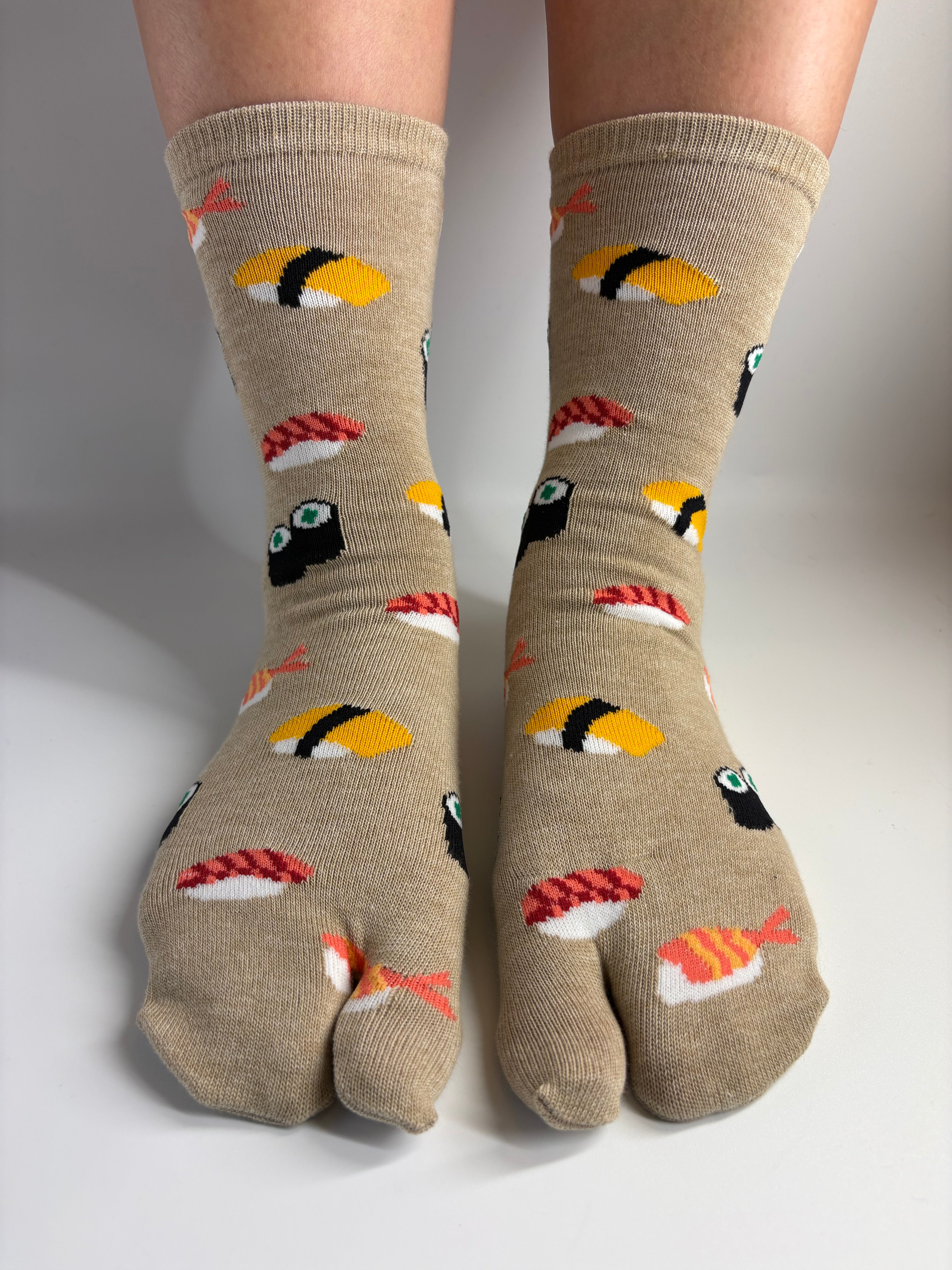 beige sushi print socks in a split toe style, work on a person's feet standing in a white background studio