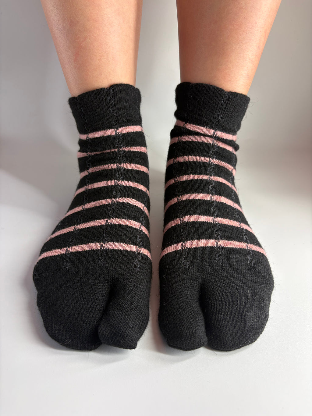 Black tabi socks with thin pink horizontal stripes, worn on feet against a plain white background.