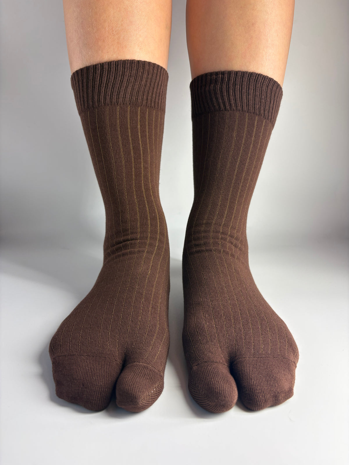 A pair of dark brown ribbed crew socks worn on a person's feet, shown against a plain light gray background.