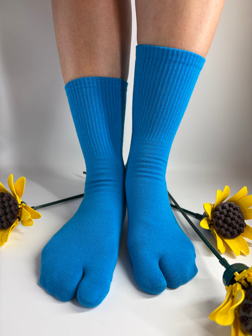 A pair of bright blue toe socks worn on feet, shown from above on a light background with yellow sunflower props.