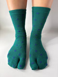 Tabi Co. dark green split-toe cotton socks with a scattered blue number print, worn on feet