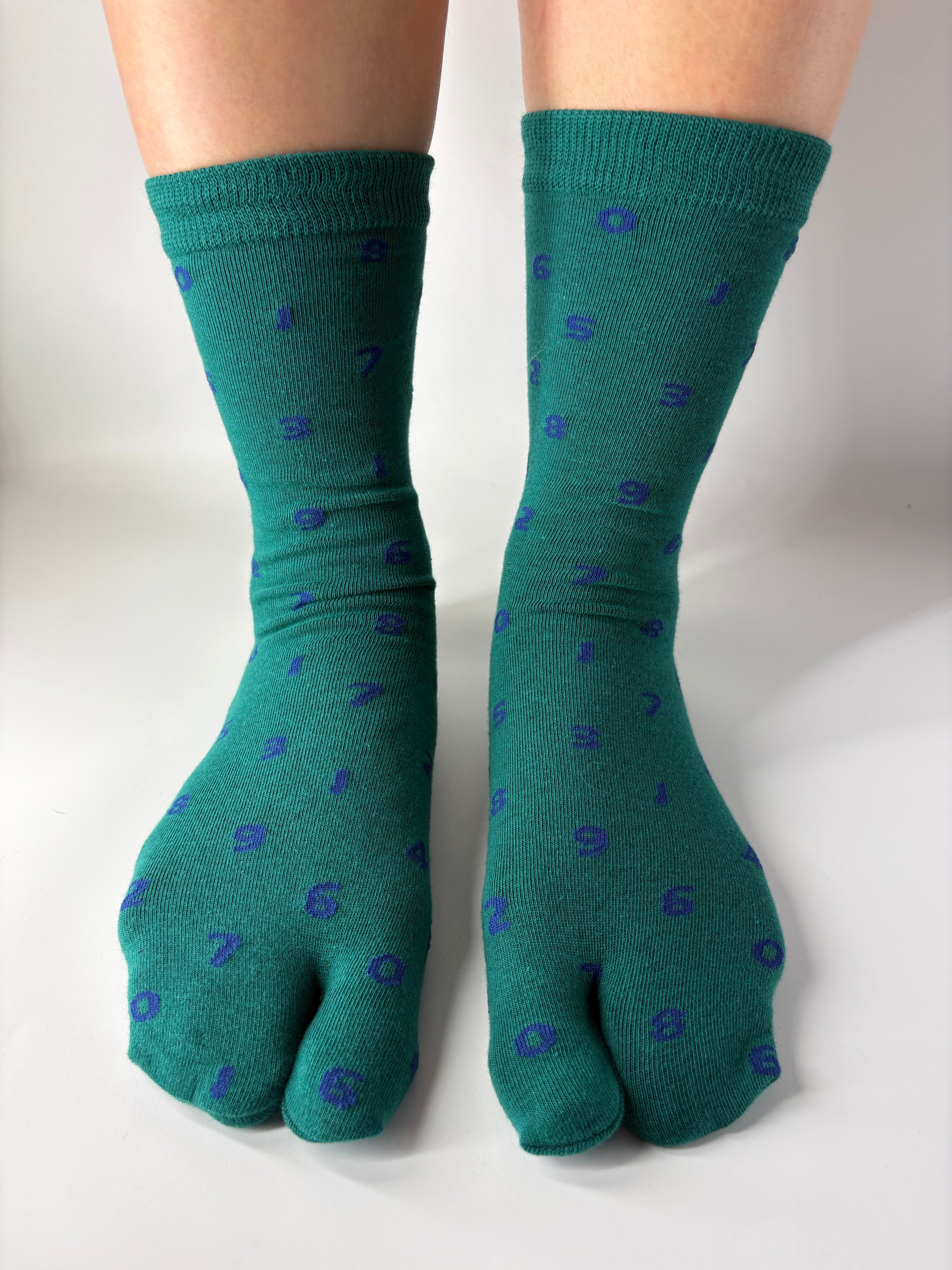 Tabi Co. dark green split-toe cotton socks with a scattered blue number print, worn on feet