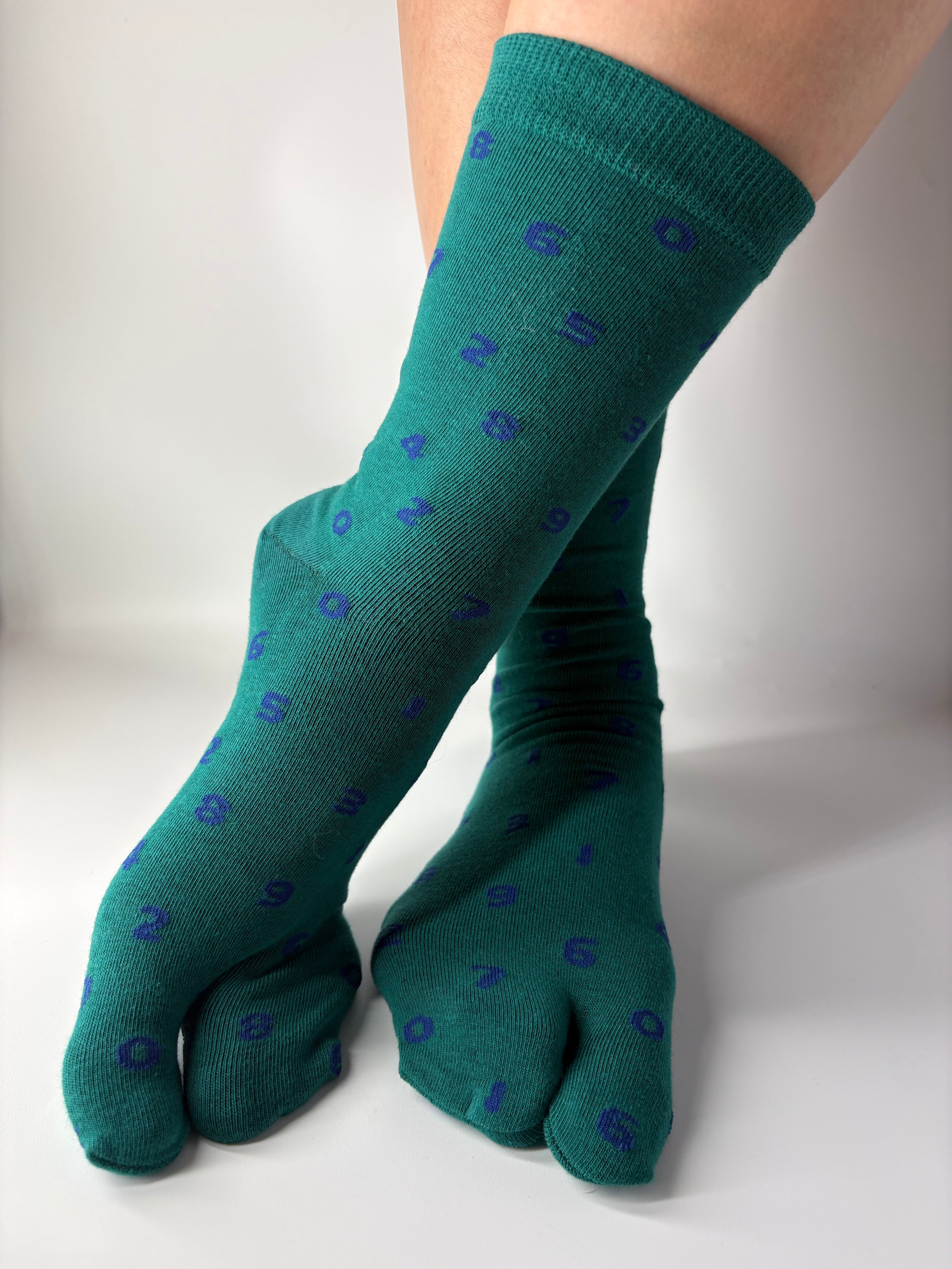 Tabi Co. dark green split-toe cotton socks with a scattered blue number print, worn on feet