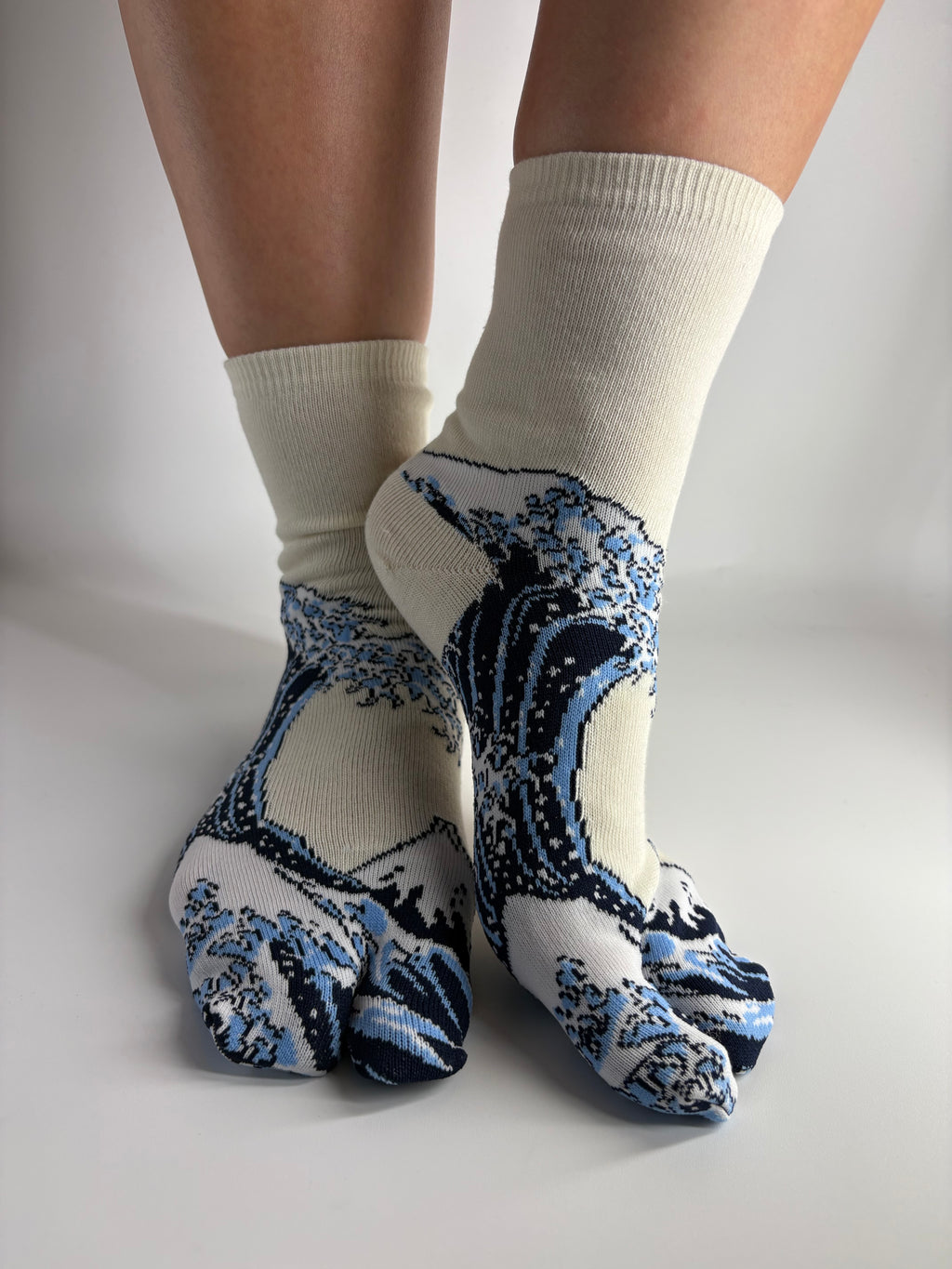 A pair of split toe crew socks with a blue and white wave pattern, worn on feet against a plain light gray background.