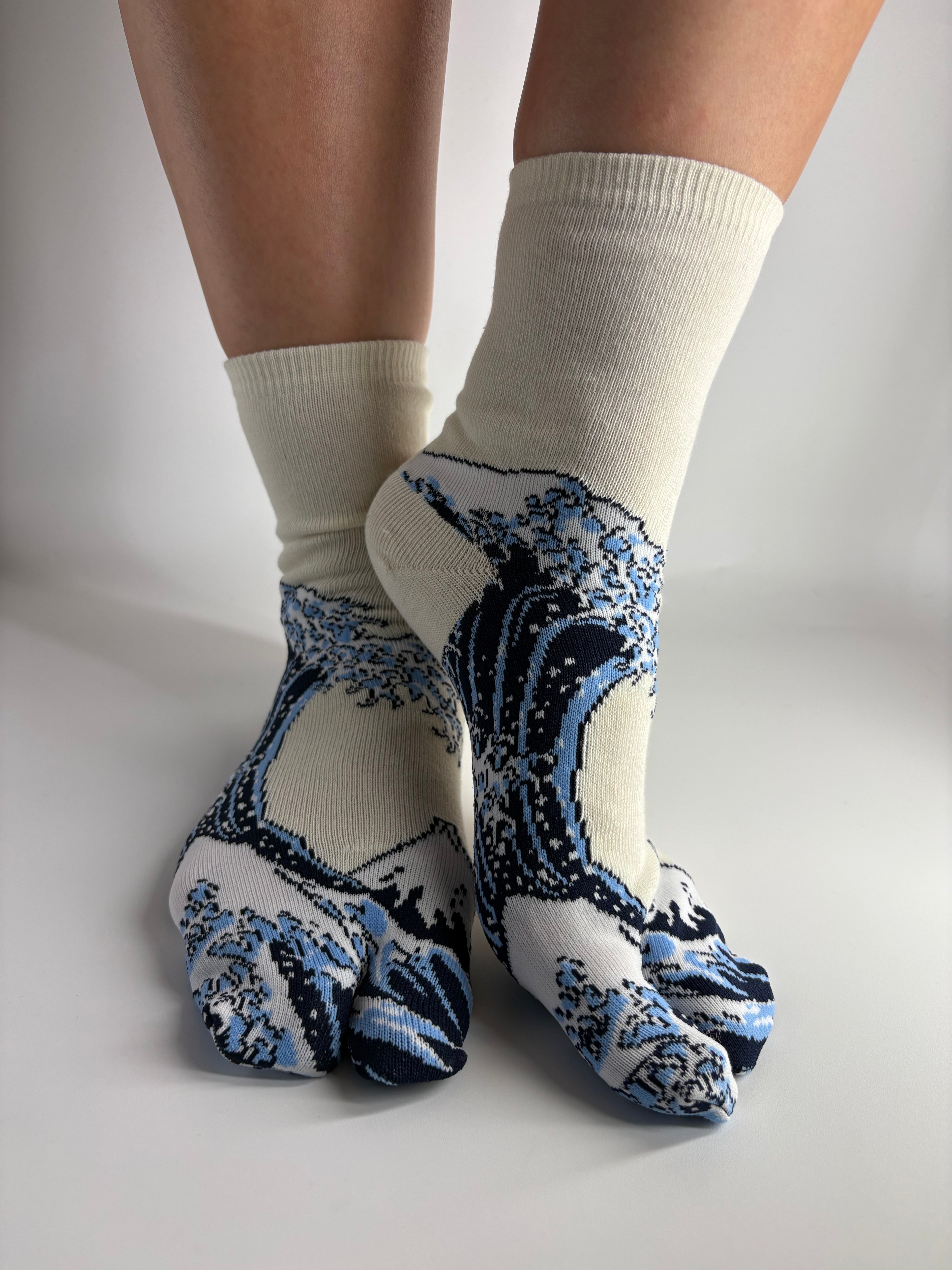 A pair of split toe crew socks with a blue and white wave pattern, worn on feet against a plain light gray background.