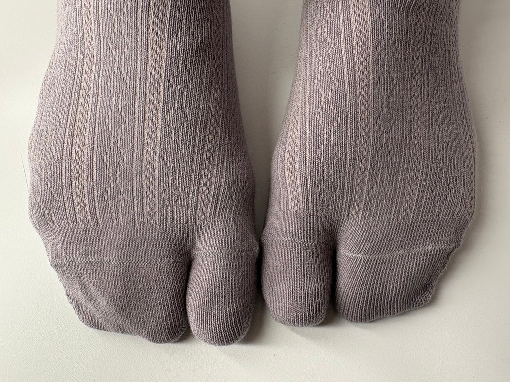 A pair of light grayish-purple ribbed split toe socks worn on feet, shown against a plain off-white background.