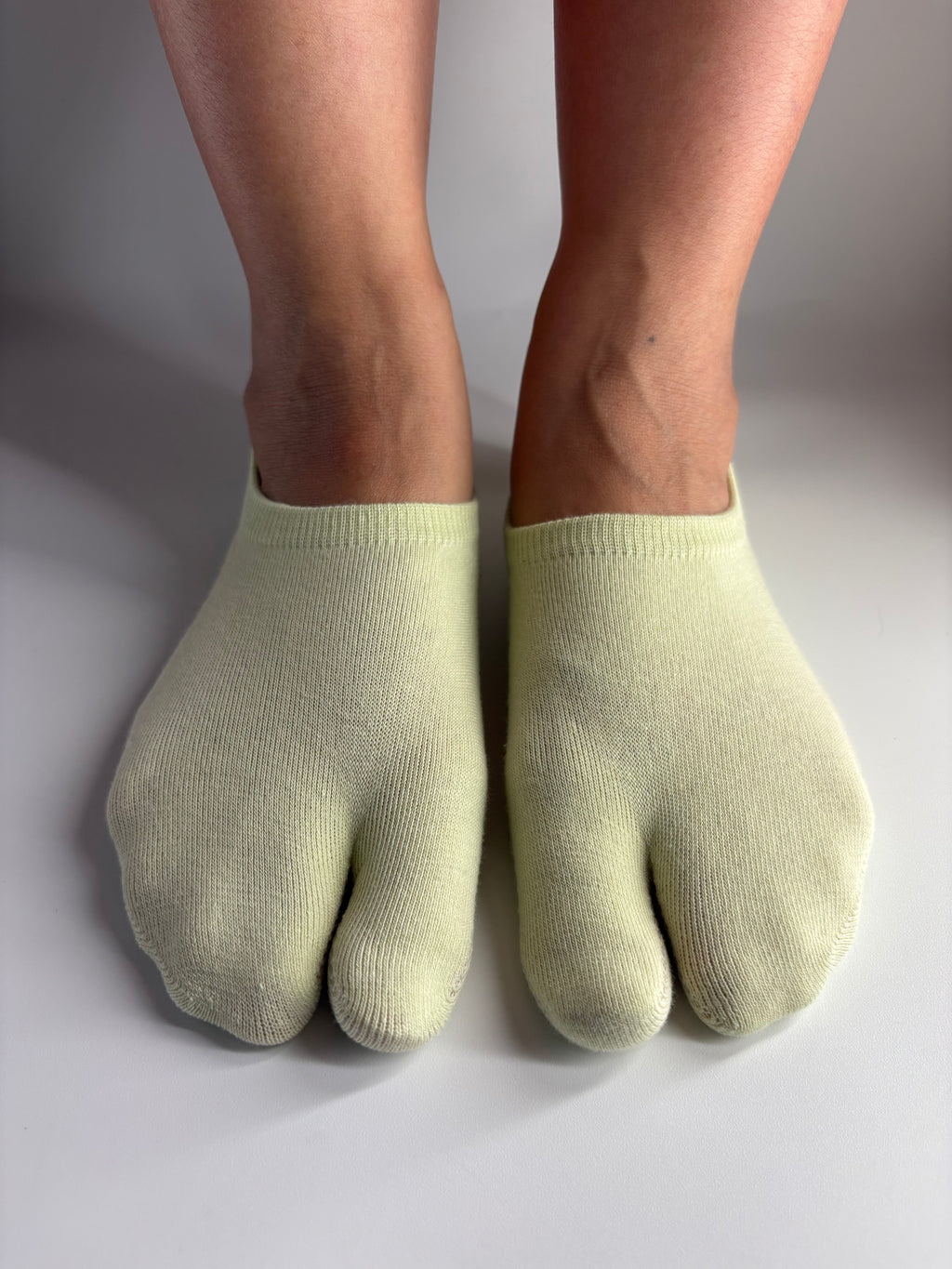 a pair of low cut ankle tabi socks in a light soft pistachio green colour standing on a white background