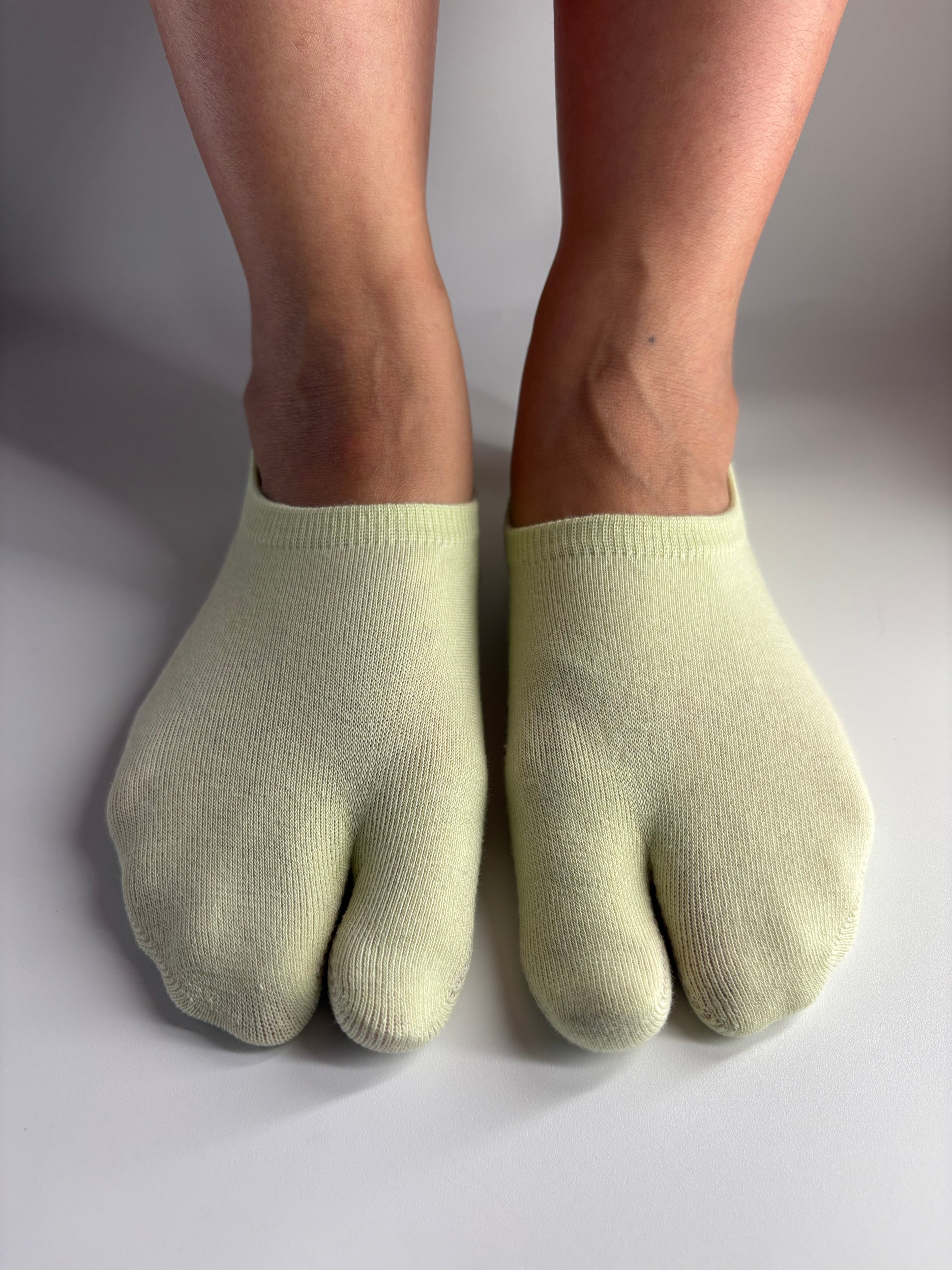 a pair of low cut ankle tabi socks in a light soft pistachio green colour standing on a white background