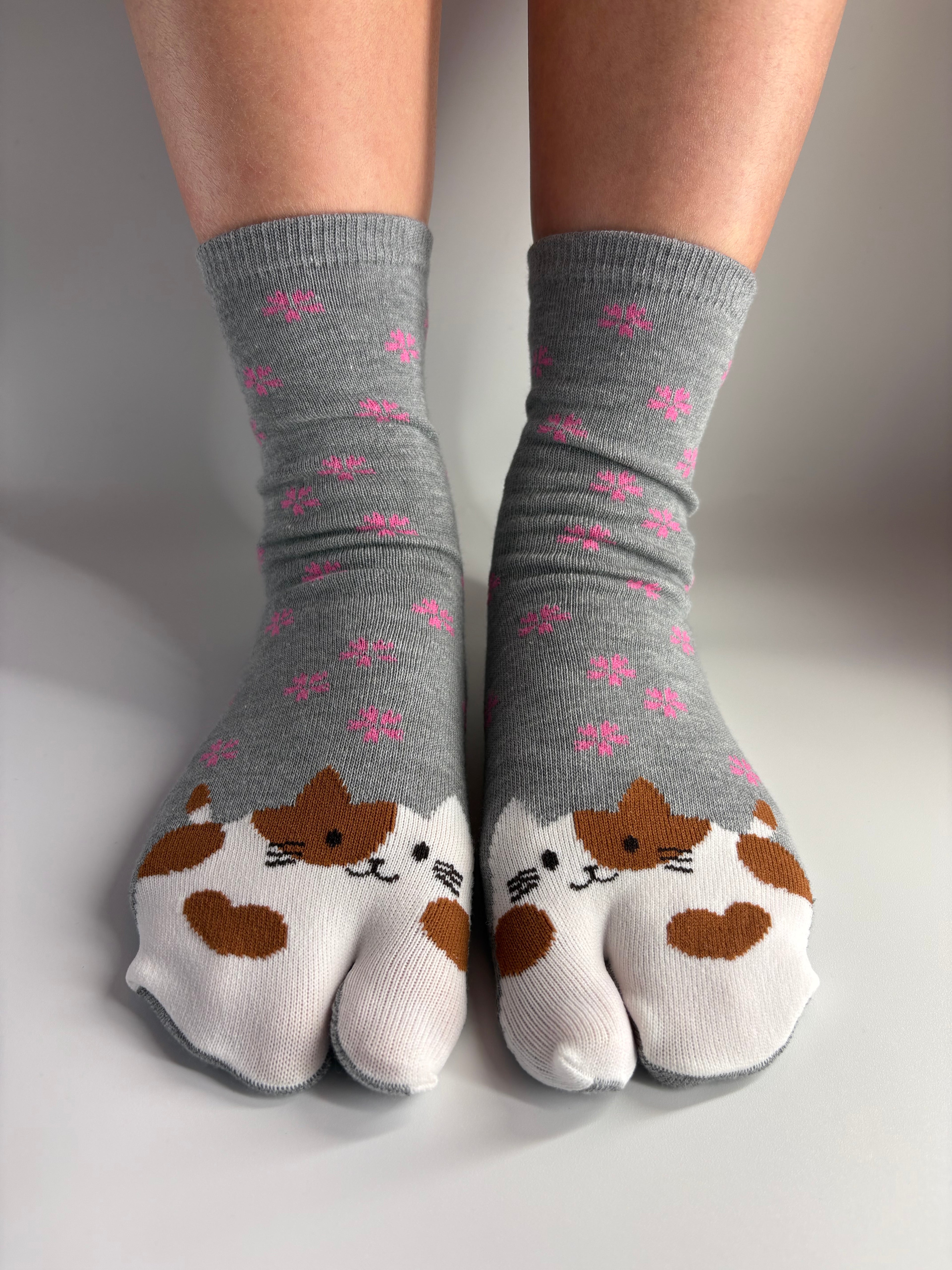 light grey tabi socks with a cat graphic print and pink floral motif, standing on white background