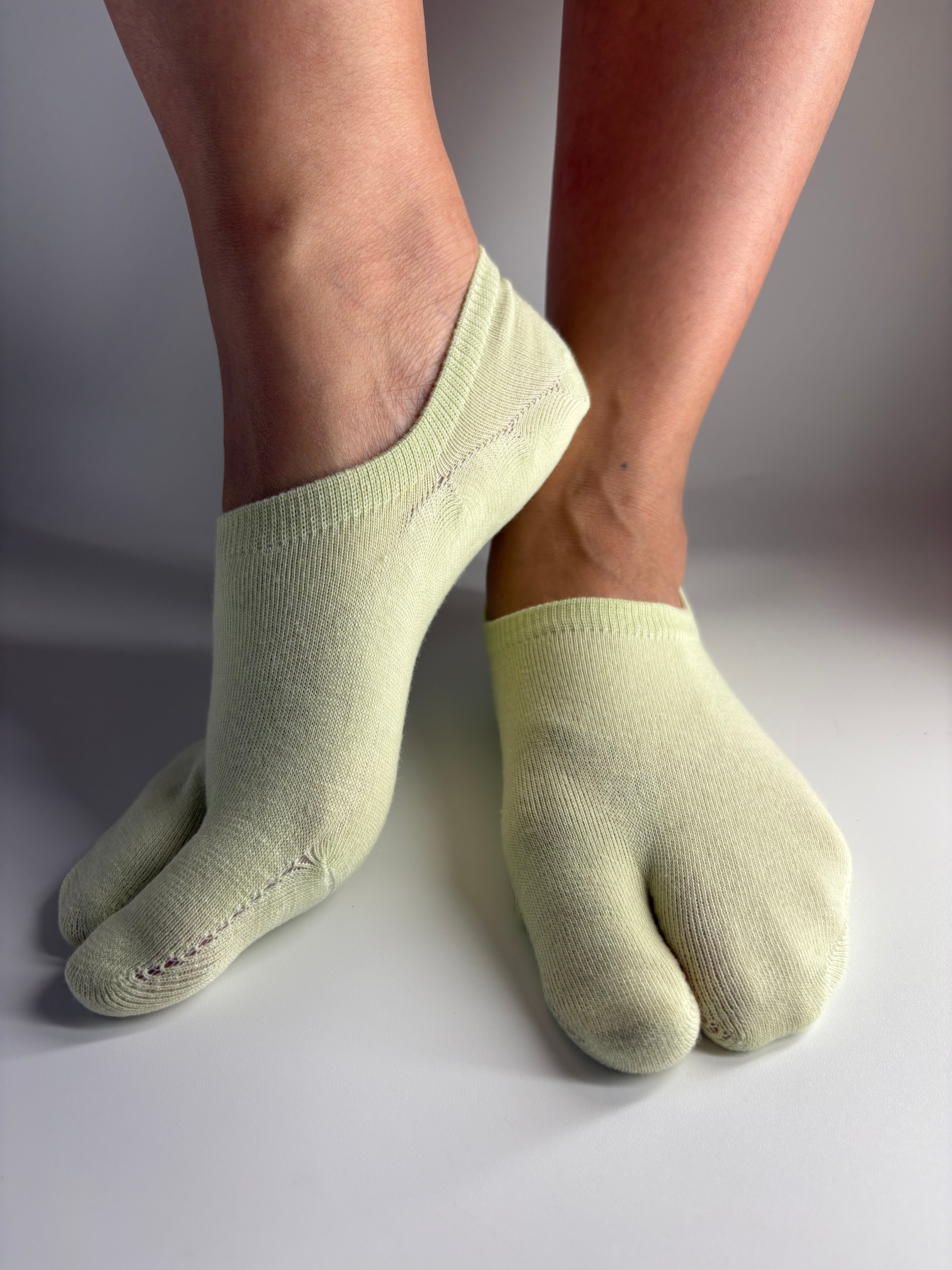 a pair of low cut ankle tabi socks in a light soft pistachio green colour standing on a white background