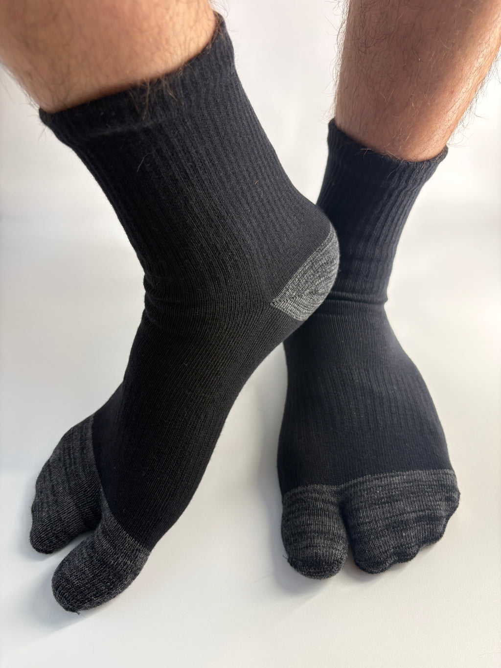 A pair of black and dark gray split-toe tabi socks worn on feet, shown against a plain white background.