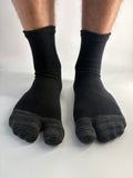 A pair of black and dark gray split-toe tabi socks worn on feet, shown against a plain white background.